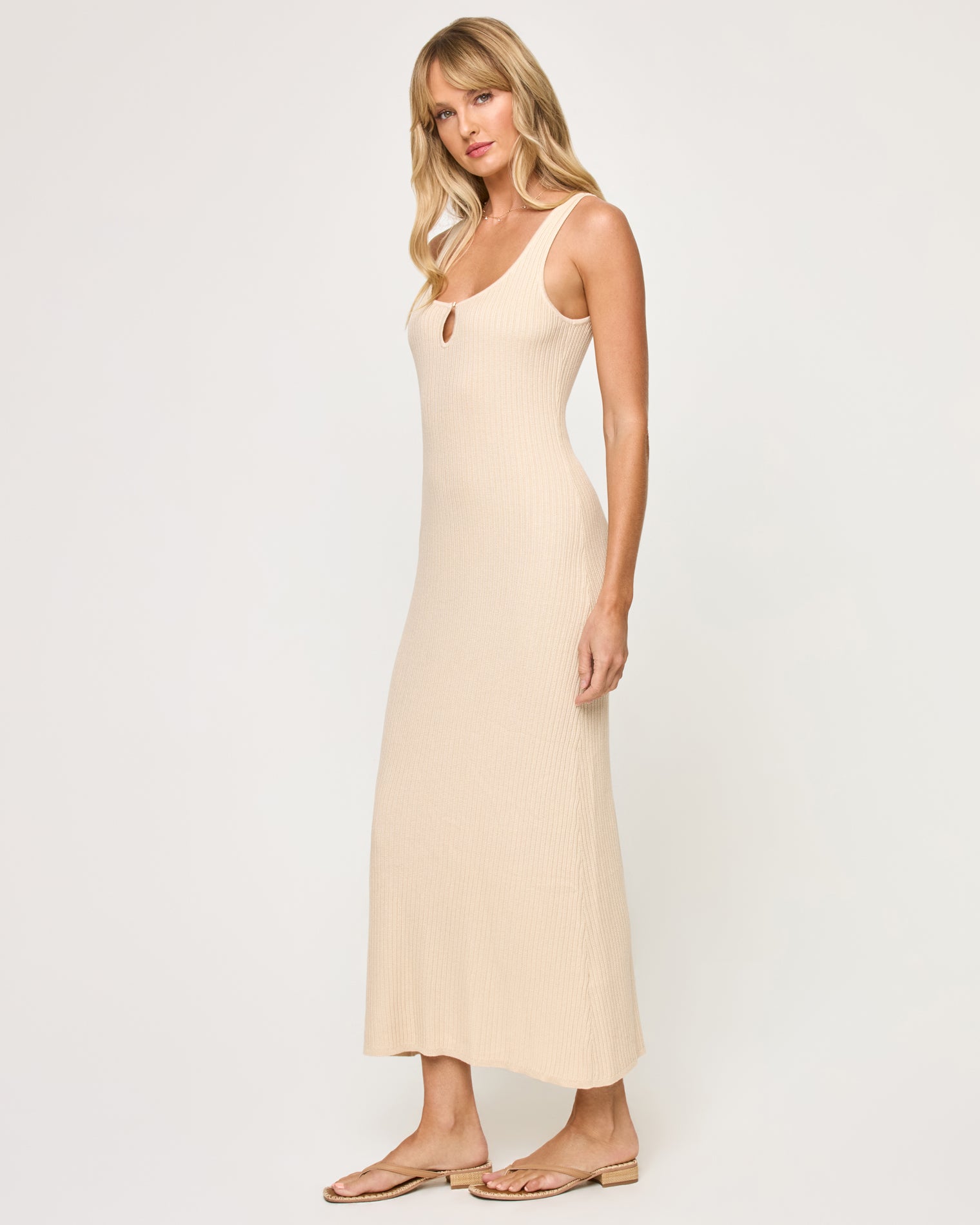 En Route Dress - Oat Side view of a model wearing the LSPACE En Route Dress - Oat in oat, showing the ribbed knit texture and slightly flared hem of the sleeveless maxi dress.