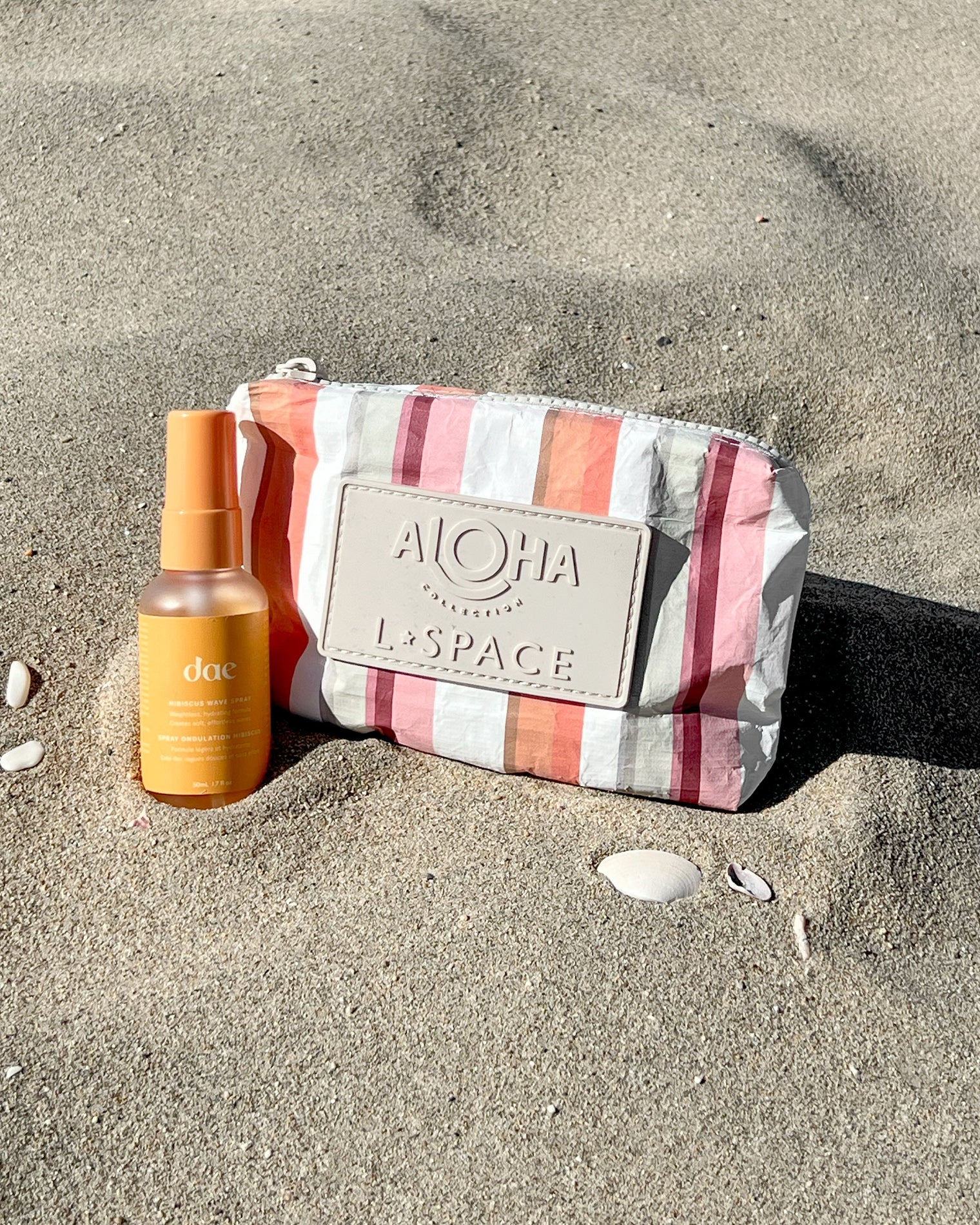 Aloha Bag + Dae Spray Gift LSPACE Aloha bag and Dae hair spray gift set in pink stripe, off-model flat lay on sand.