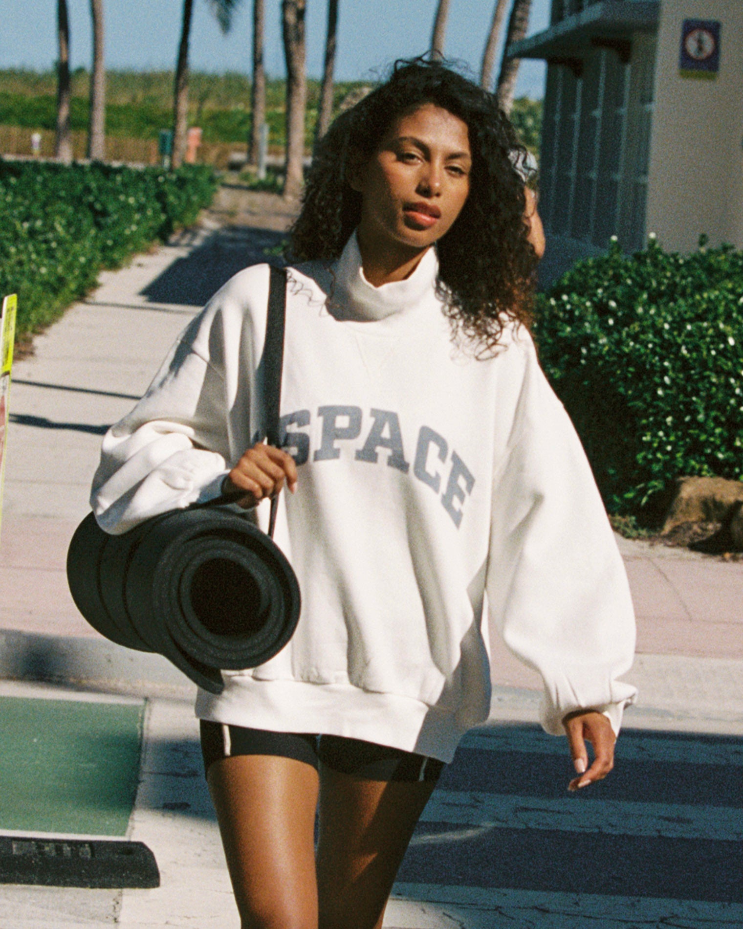 Crush Sweatshirt - Cream Outdoor lifestyle front view of the Crush Sweatshirt in cream, a cream quarter-zip pullover sweatshirt with "LSPACE" collegiate arch lettering, model carrying a yoga mat.