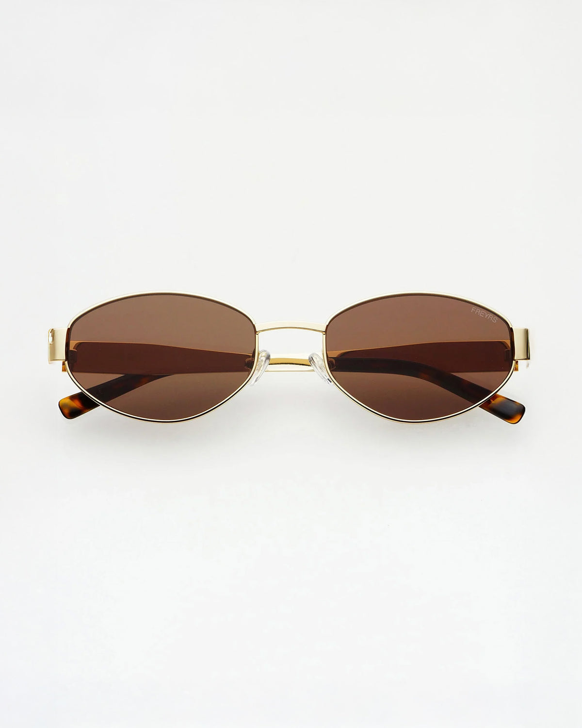 Freyrs Soho Sunglasses - Gold Oval sunglasses with brown tinted lenses, a thin gold metal frame, and tortoiseshell temple tips, shown against a plain white background.