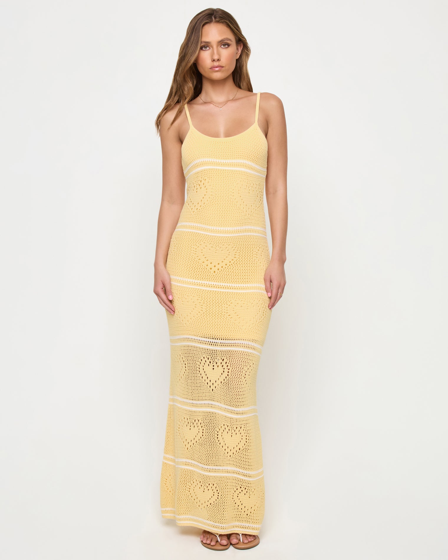 Heart To Heart Dress - Daisy-Cream Front view of a model wearing the LSPACE Heart To Heart Dress in daisy-cream, featuring the body-hugging open-knit crochet maxi silhouette in soft yellow with horizontal cream stripe details and heart motifs throughout, scoop neckline, and thin spaghetti straps, against a white studio background.