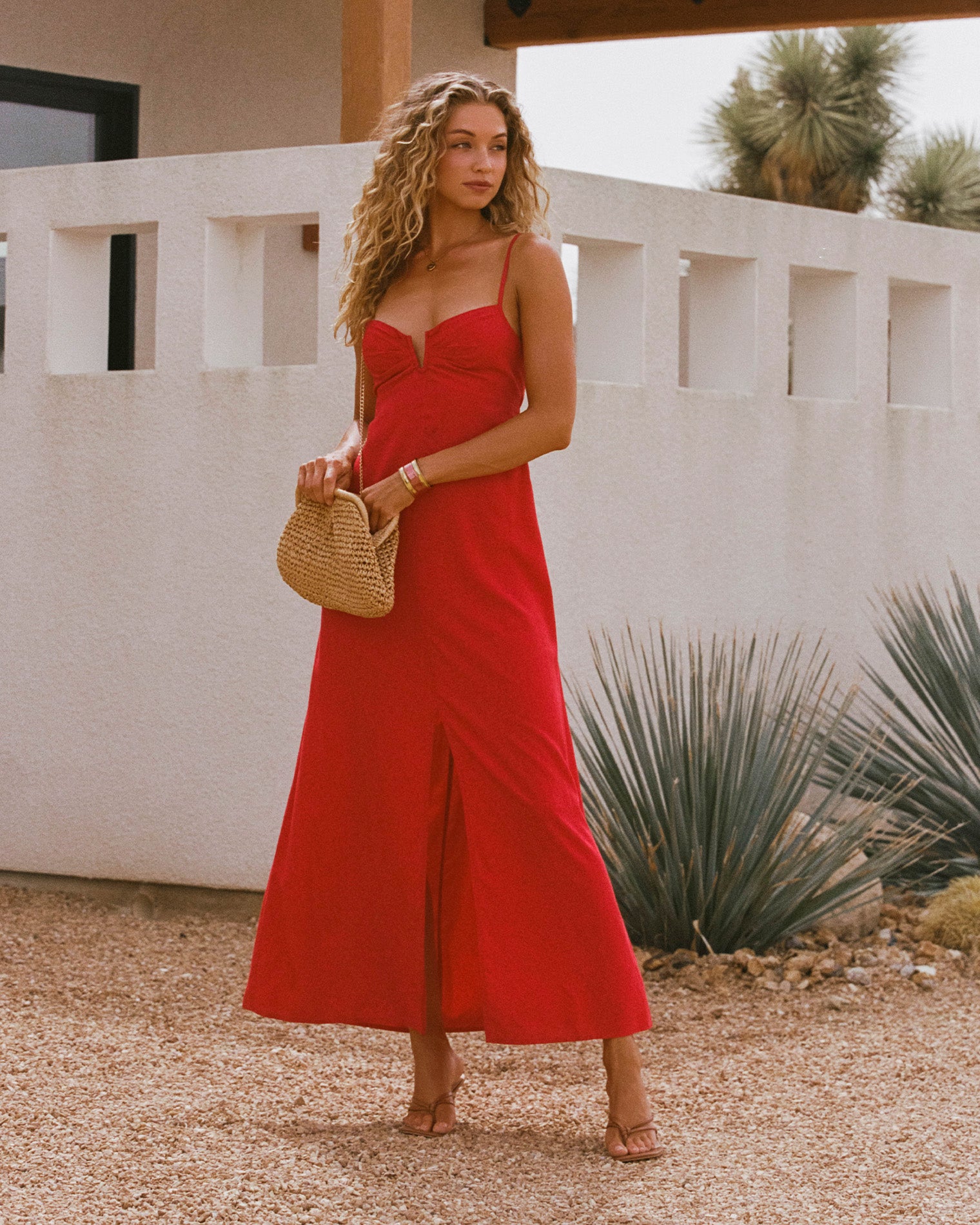 Chara Maxi Dress - Lipstick Red Lipstick Red | Badge:New Arrival_#B2AC88_#ffffff'
Lifestyle image of model wearing the LSPACE Chara Maxi Dress in lipstick red, a floor-length spaghetti-strap maxi dress with a bustier-style neckline and front slit, outdoors against a white stucco wall.
