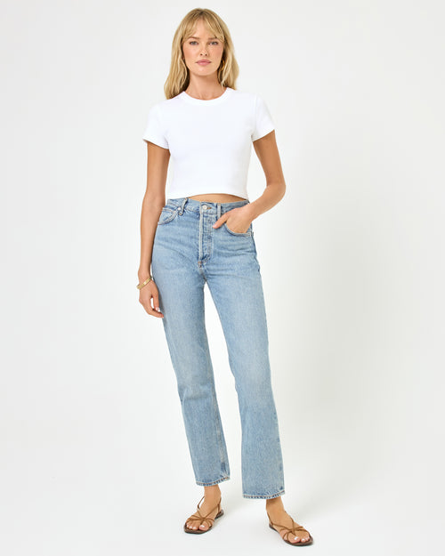 Full-length front view of a model wearing the LSPACE Julia Top in white, a fitted white crew-neck short-sleeve crop top, styled with light blue jeans and strappy flat sandals on a white background.