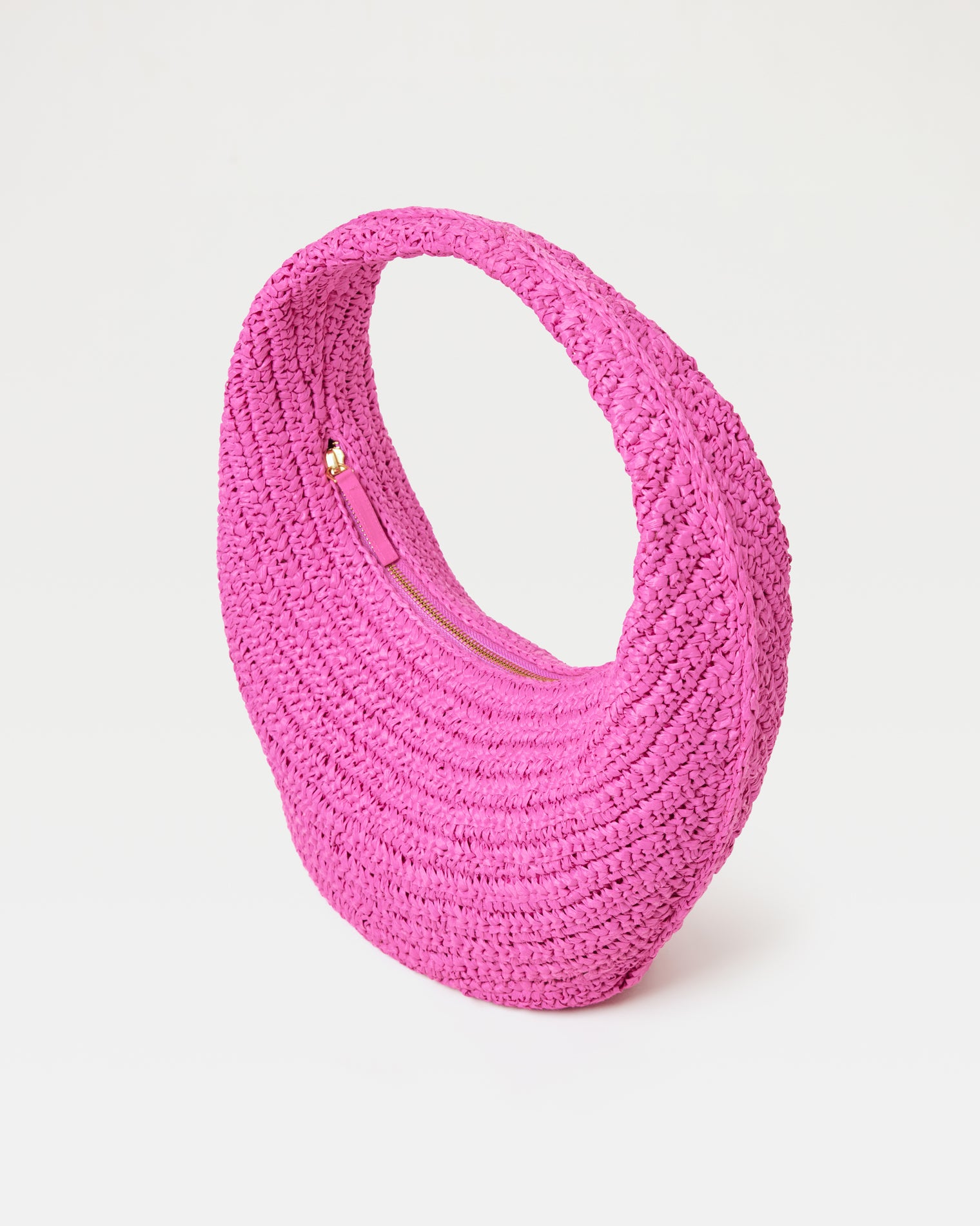 Aya Bag - Bubblegum Pink Angled view of the Aya Bag in bubblegum pink, a crescent-shaped woven raffia hobo bag, with gold zipper closure.