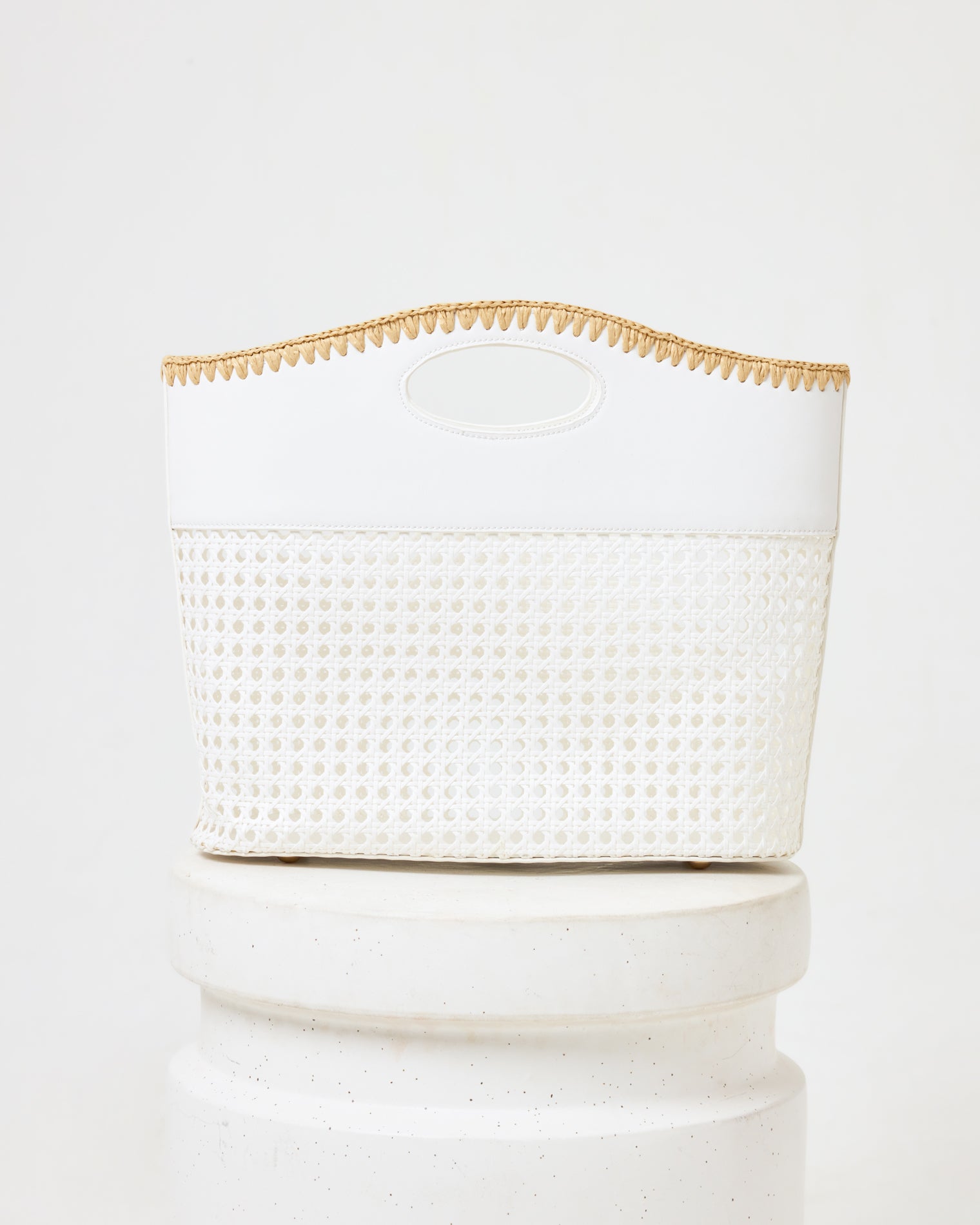 Casablanca Bag - Cream Off-model image of the Casablanca Bag in cream, a structured bag with a rattan weave bottom, cream fabric top, oval cutout handle, and natural trim, on a white pedestal.