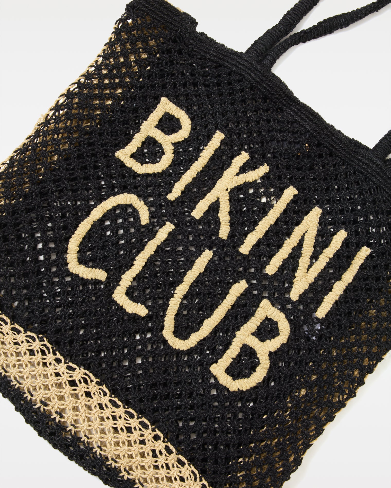 Moonlight Bag - Natural-Black Close-up of the Moonlight Bag in natural-black showing the 'Bikini Club' intarsia lettering detail on the open-weave crochet body.