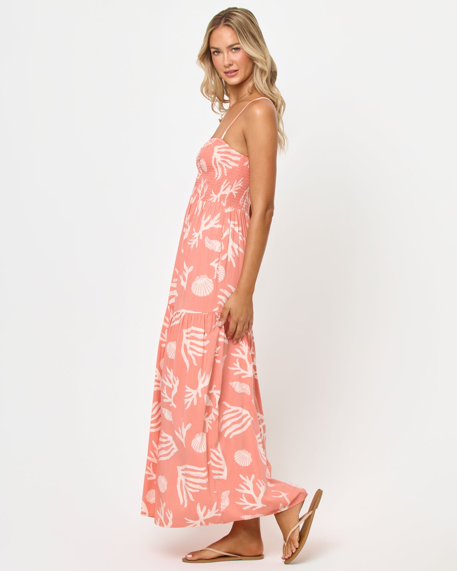 Mallorca Dress - Shell Or High Water Side view of a model wearing the LSPACE Mallorca Dress in Shell Or High Water, showing the silhouette of the smocked bodice and tiered maxi skirt in the coral shell and reef print.