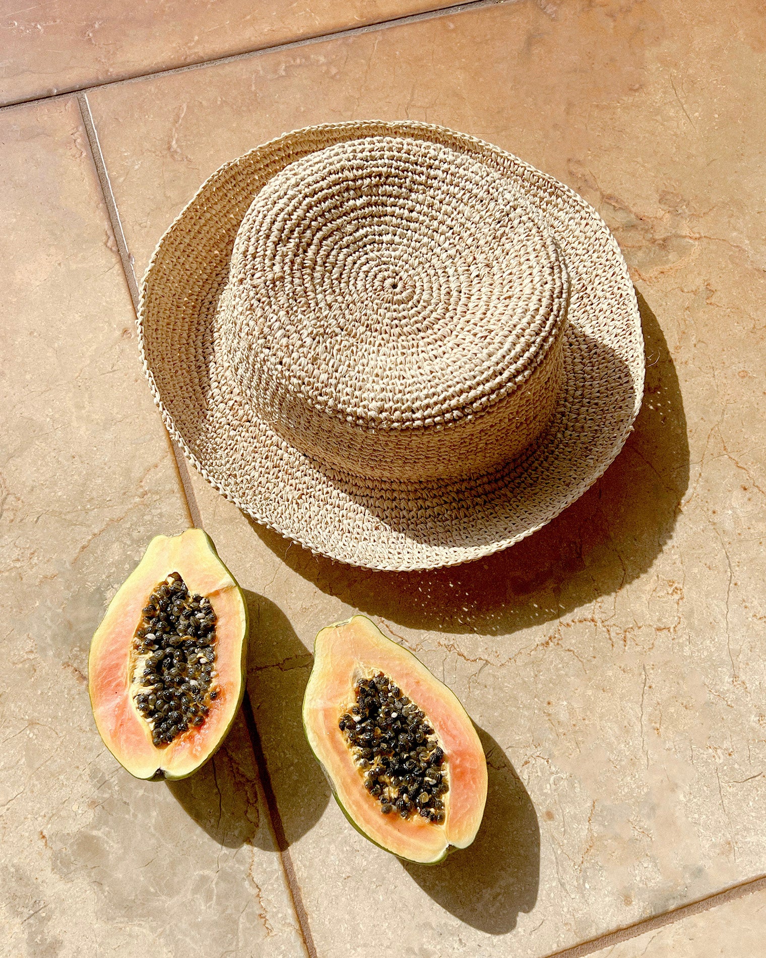 Isadora Bucket Hat - Natural Flat lay of the Isadora Bucket Hat in natural styled with tropical fruits on a terracotta tile.