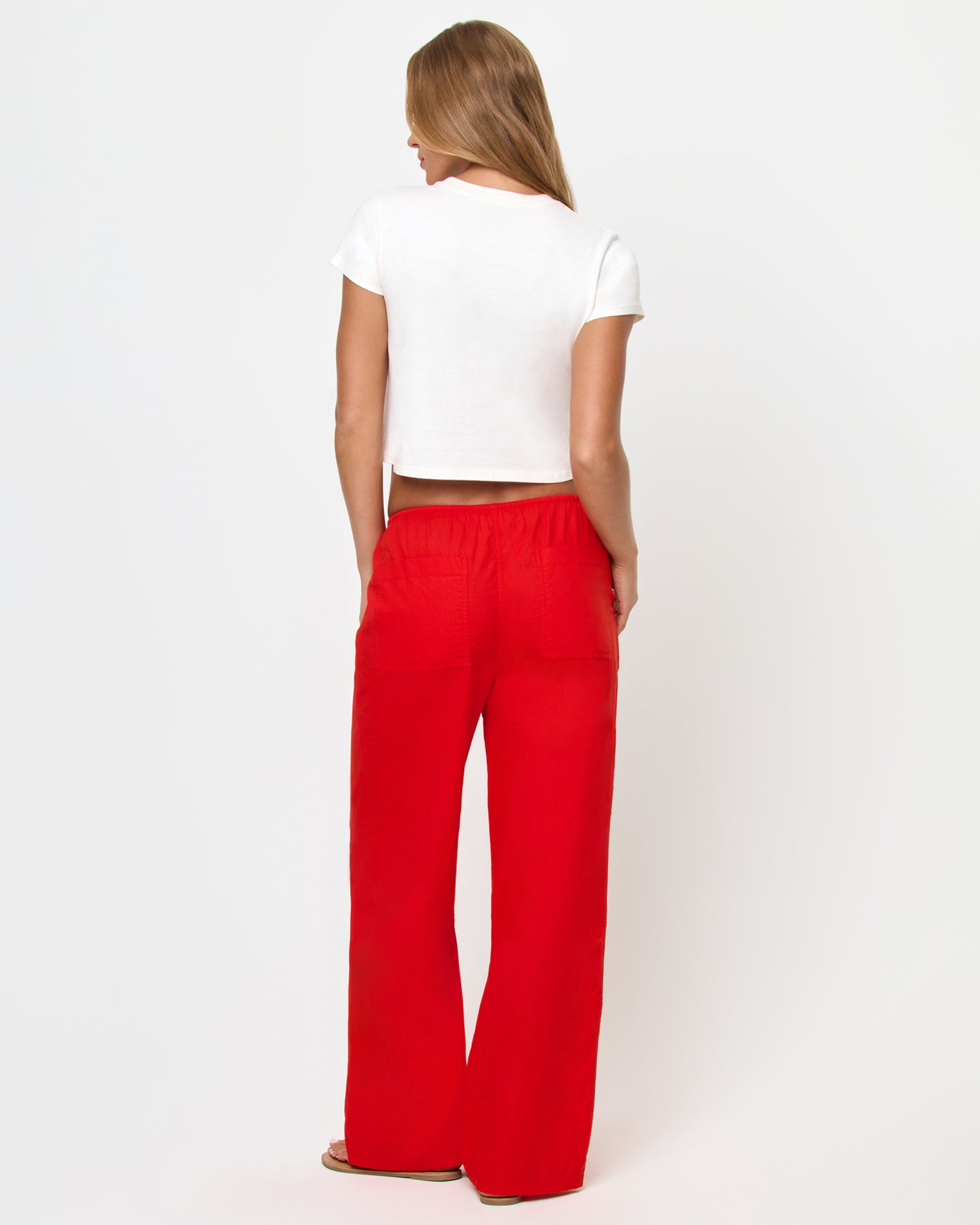 Merci Baby Tee - Shrimp Back view of a model wearing the LSPACE Merci Baby Tee in Shrimp, showing the plain white cropped back, styled with red wide-leg drawstring pants.