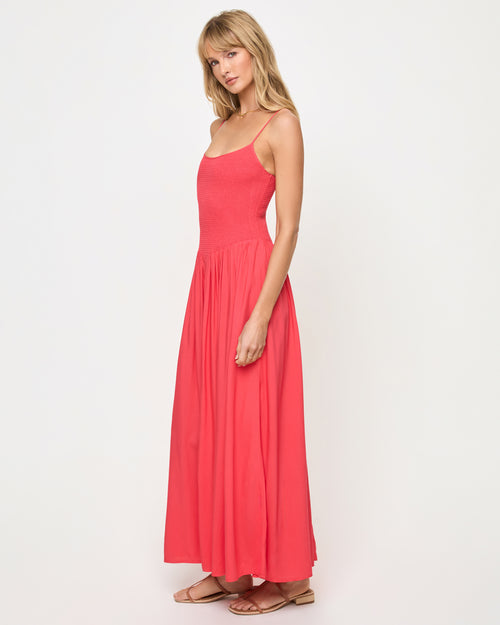 Side view of a model wearing the LSPACE Misha Midi in pout, showing thin spaghetti straps, a smocked bodice, and a full flowing coral pink skirt.