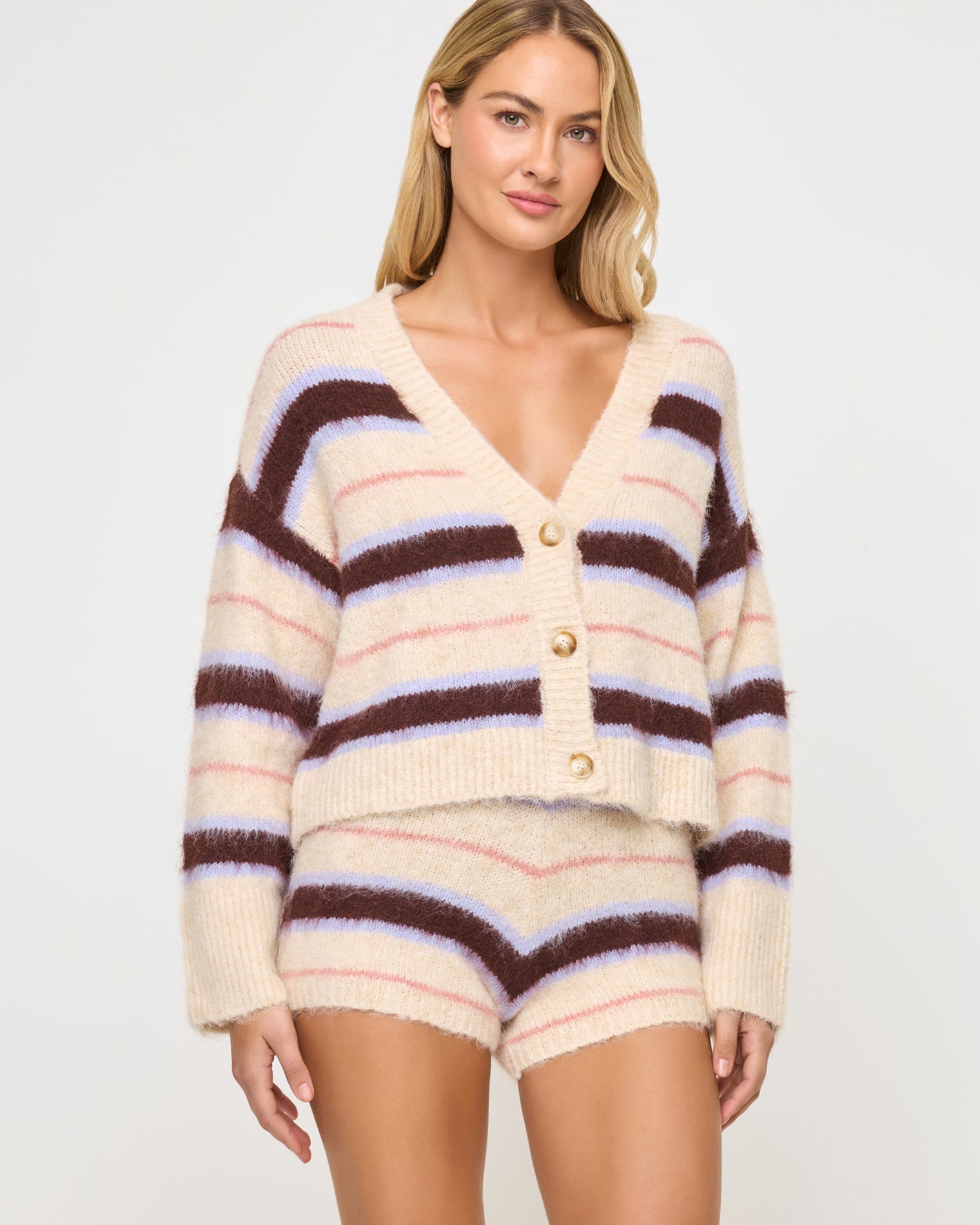 Montauk Cardigan - Prep School Stripe Full-length front view of a model wearing the LSPACE Montauk Cardigan in prep school stripe, a cropped oversized V-neck button-front cardigan in a soft eyelash knit with wavy horizontal stripes in cream, dark brown, lavender, and pink, styled with the matching Montauk Short.