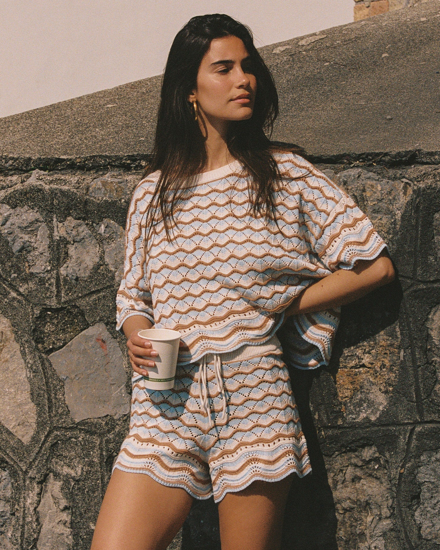 Sunchaser Top - North Shores Angled view of a model wearing the LSPACE Sunchaser Top in north shores, a boxy crochet knit top with short sleeves and a wave scallop pattern in light blue and tan, photographed outdoors, styled with the matching shorts.