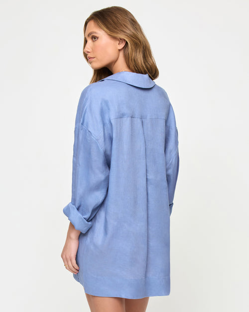 Back view of a model wearing the LSPACE Oasis Tunic in chambray, showing a collared neckline, long sleeves with rolled cuffs, a center back panel, and a relaxed oversized silhouette.