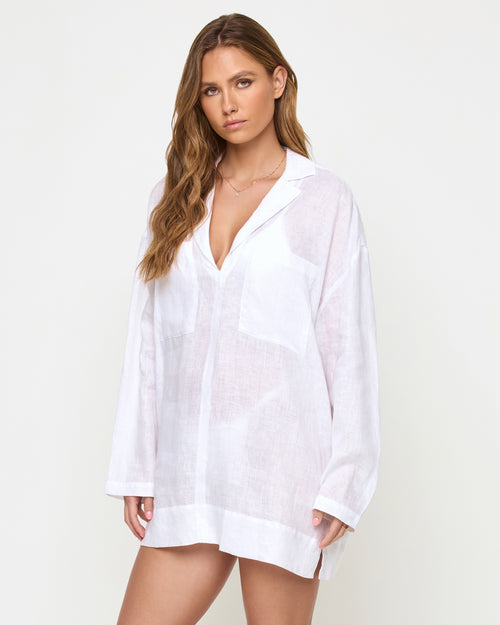 Three-quarter view of a model wearing the LSPACE Oasis Tunic in white, showing the semi-sheer linen fabric, open V-neckline, and long-sleeve oversized relaxed fit.