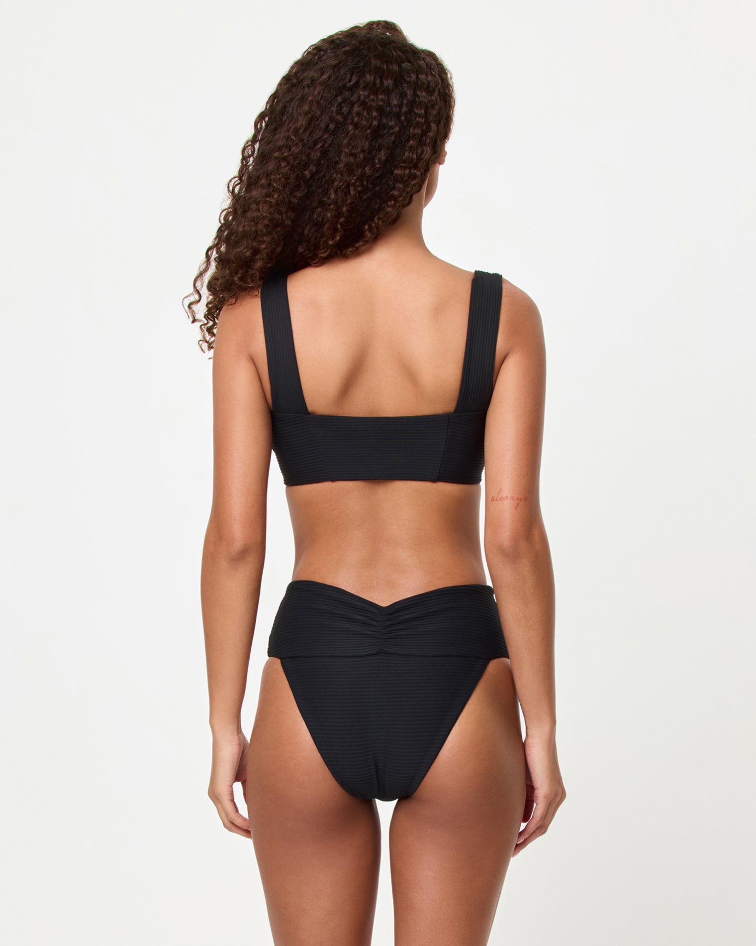 Marlee Bikini Top - Black Back view of a model wearing the LSPACE black Bardot Bikini Bottom, a ribbed high-waist style showing the gathered center back waistband detail, paired with the black Marlee Bikini Top.