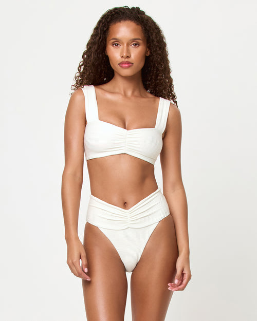 Front view of a model wearing the LSPACE ribbed cream Marlee Bikini Top, a bralette style with wide straps and gathered center front detail, paired with the matching Bardot Bikini Bottom.