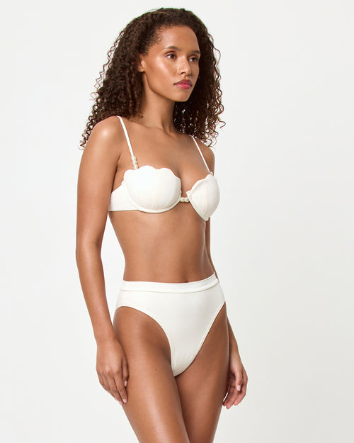 Side view of a model wearing the LSPACE cream Frenchi Bikini Bottom, a high-cut style with a fold-over waistband, paired with the cream Sunrise Shell Bikini Top.