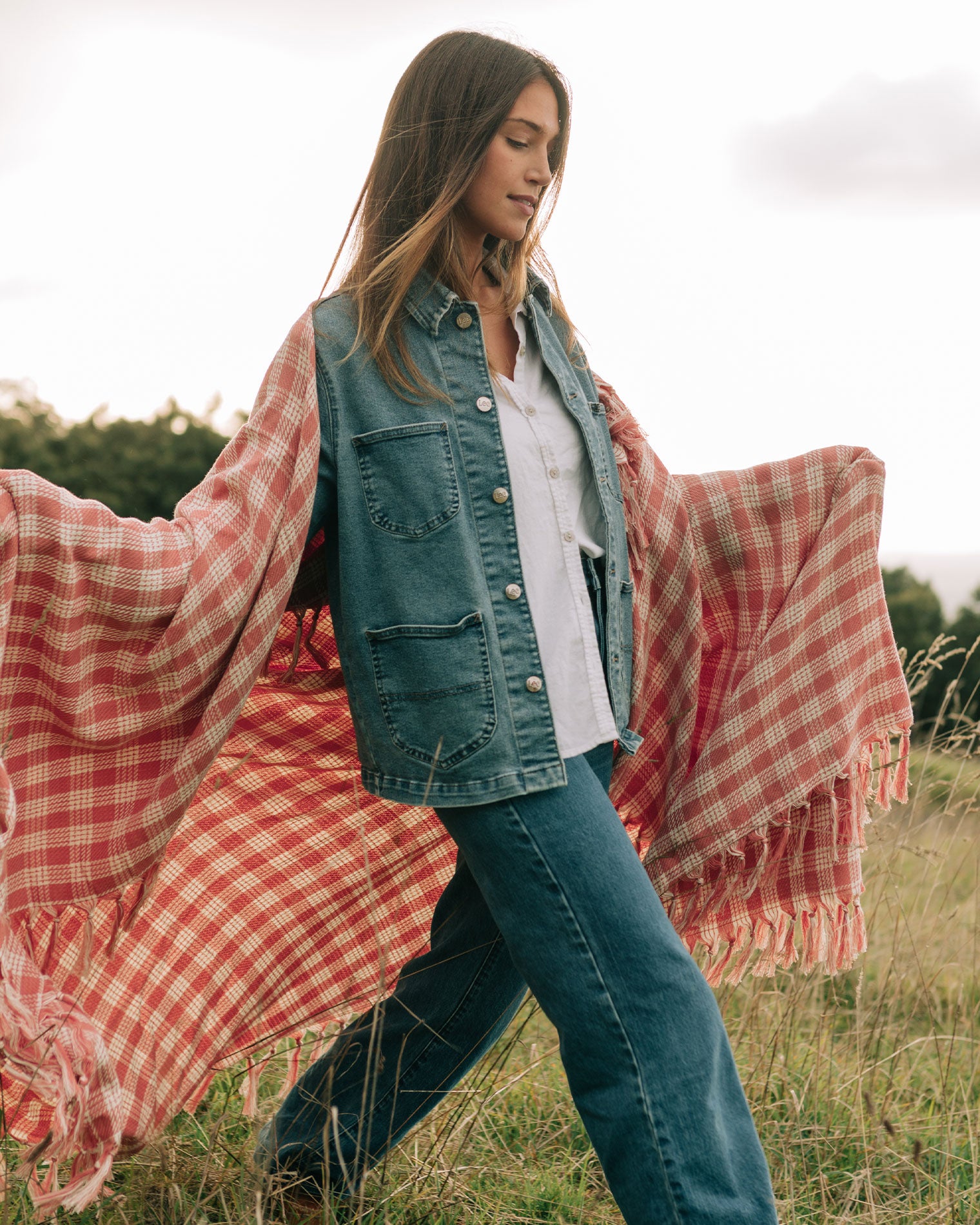 Slowtide Palaka Lightweight Beach Blanket - Guava Model holding the Slowtide Palaka Lightweight Beach Blanket in guava open in a field, wearing jeans and a denim vest.