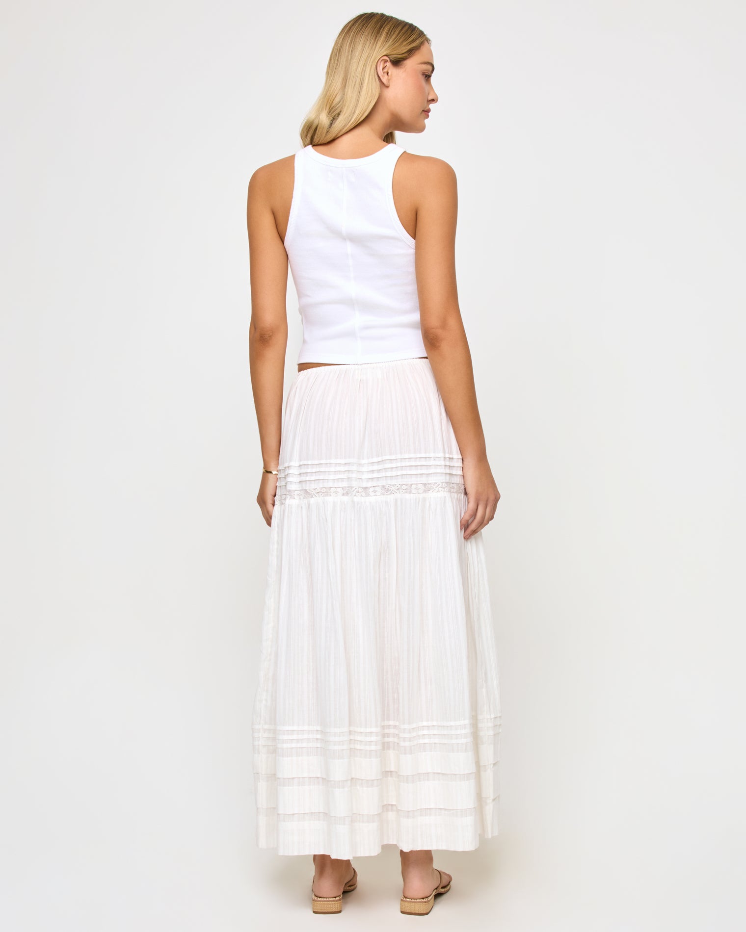 Reia Skirt - White Back view of a model wearing the LSPACE Reia Skirt in white, showing the back of the tiered maxi skirt with pin-tuck and lace trim detail, styled with a white crop top, on a white studio background.