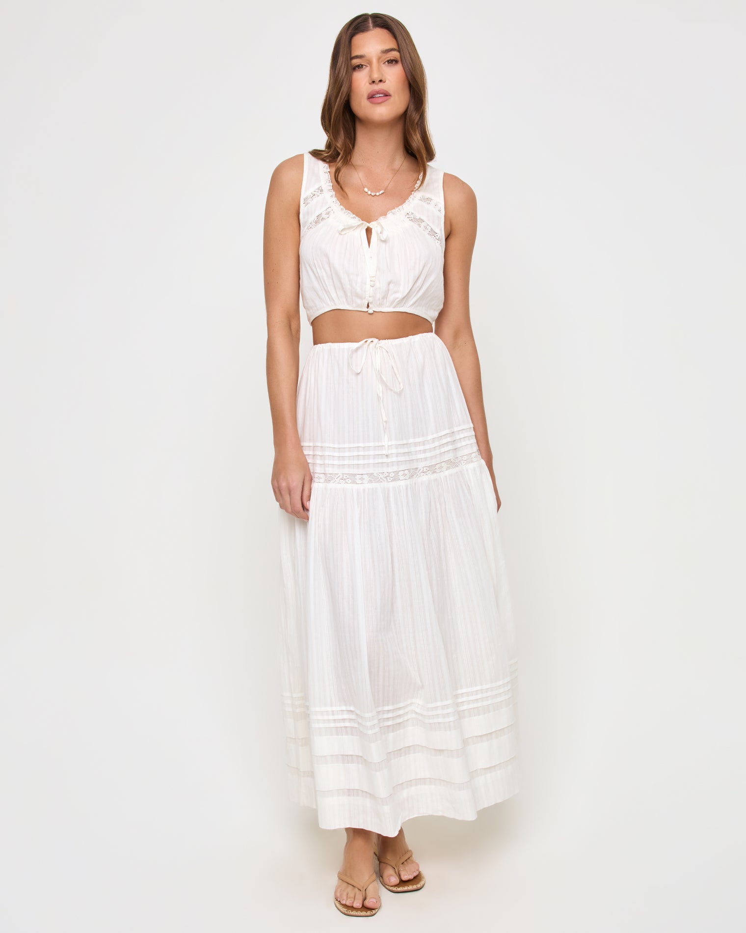 Reia Top - White Front view of a model wearing the LSPACE Reia Top in white, a sleeveless tie-front crop top with lace trim, styled with the matching white tiered maxi skirt, on a white studio background.