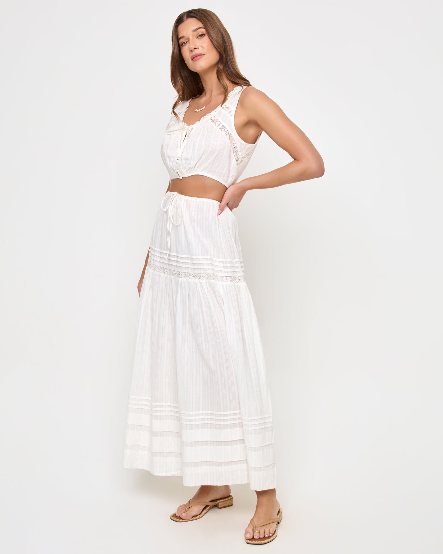Reia Top - White Three-quarter view of a model wearing the LSPACE Reia Top in white, a sleeveless tie-front crop top with lace trim, styled with the matching white tiered maxi skirt, on a white studio background.