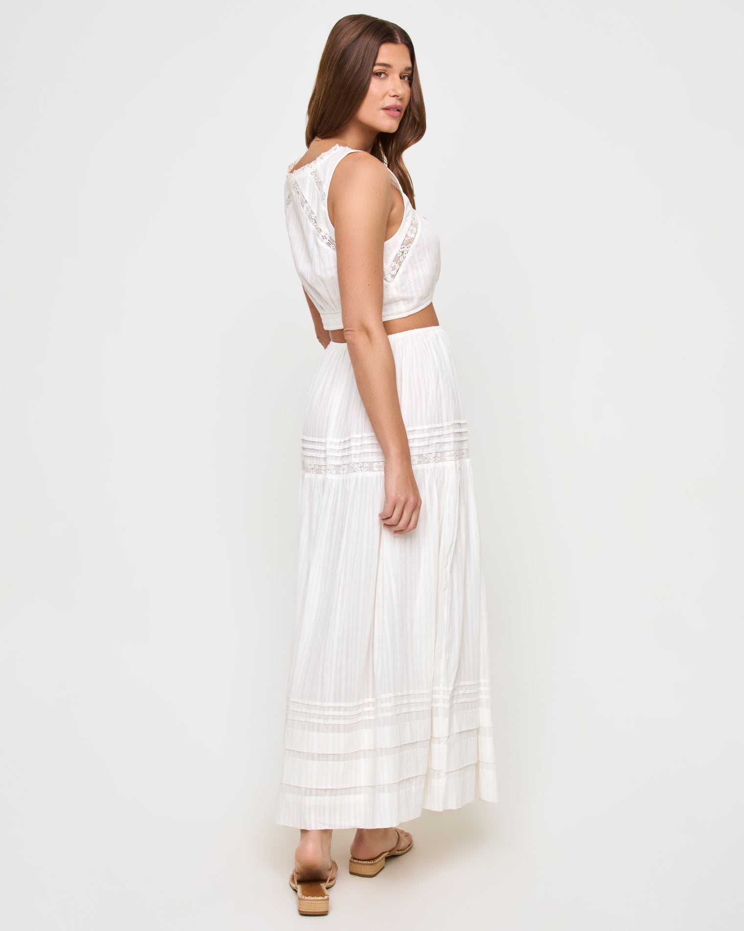 Reia Top - White Three-quarter back view of a model wearing the LSPACE Reia Top in white, showing the lace back panel detail, styled with the matching white tiered maxi skirt, on a white studio background.