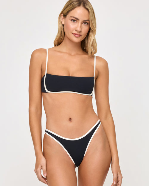 Front view of a model wearing the LSPACE black-cream Hazel Bikini Top and Elle Bikini Bottom, a square-neck bandeau bralette style with thin straps and cream contrast trim detailing.