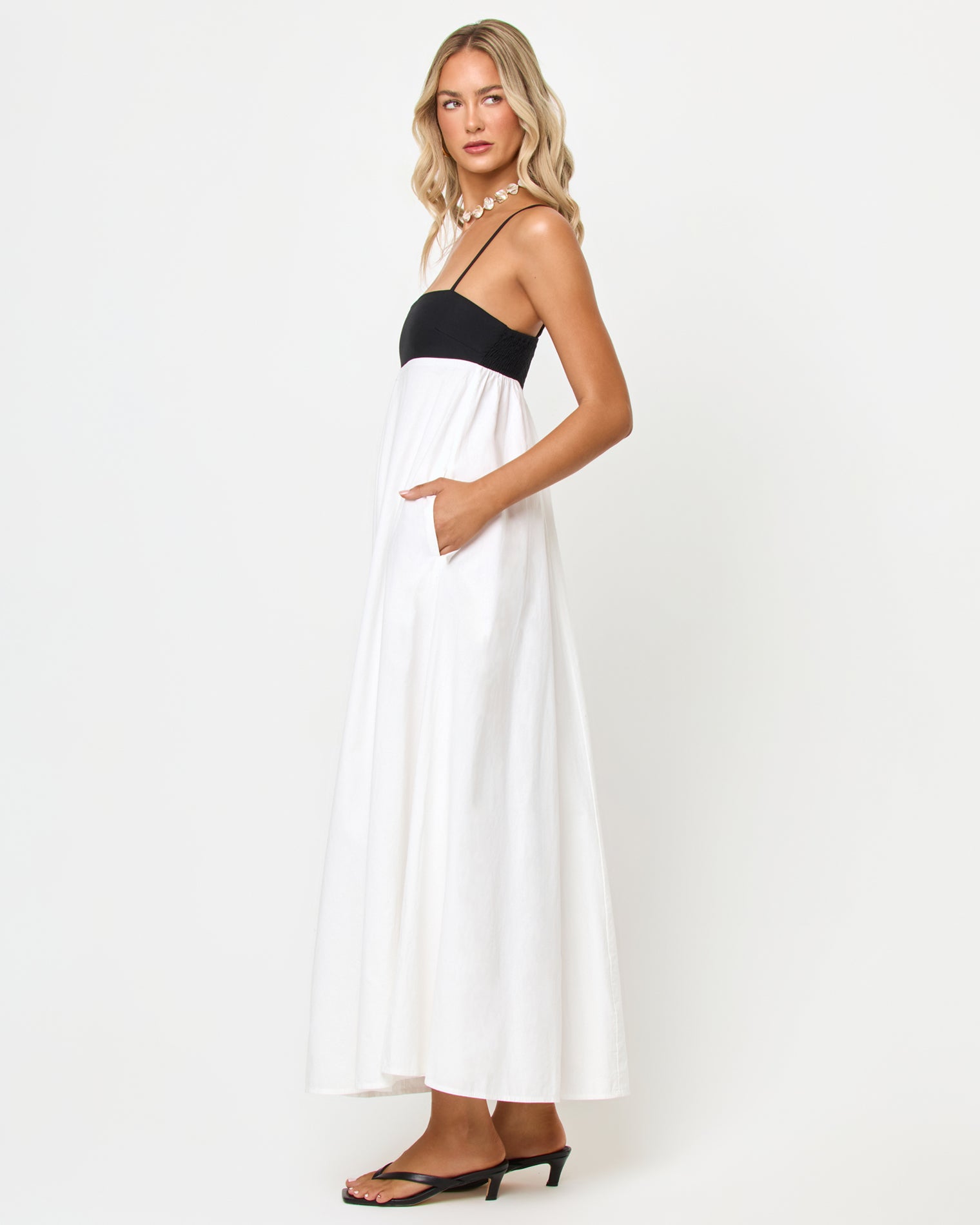 Raveena Dress - Black-Cream Side view of a model wearing the LSPACE Raveena Dress in black-cream, showing the empire-waist silhouette with a black bodice, spaghetti straps, and a flowing cream maxi skirt.