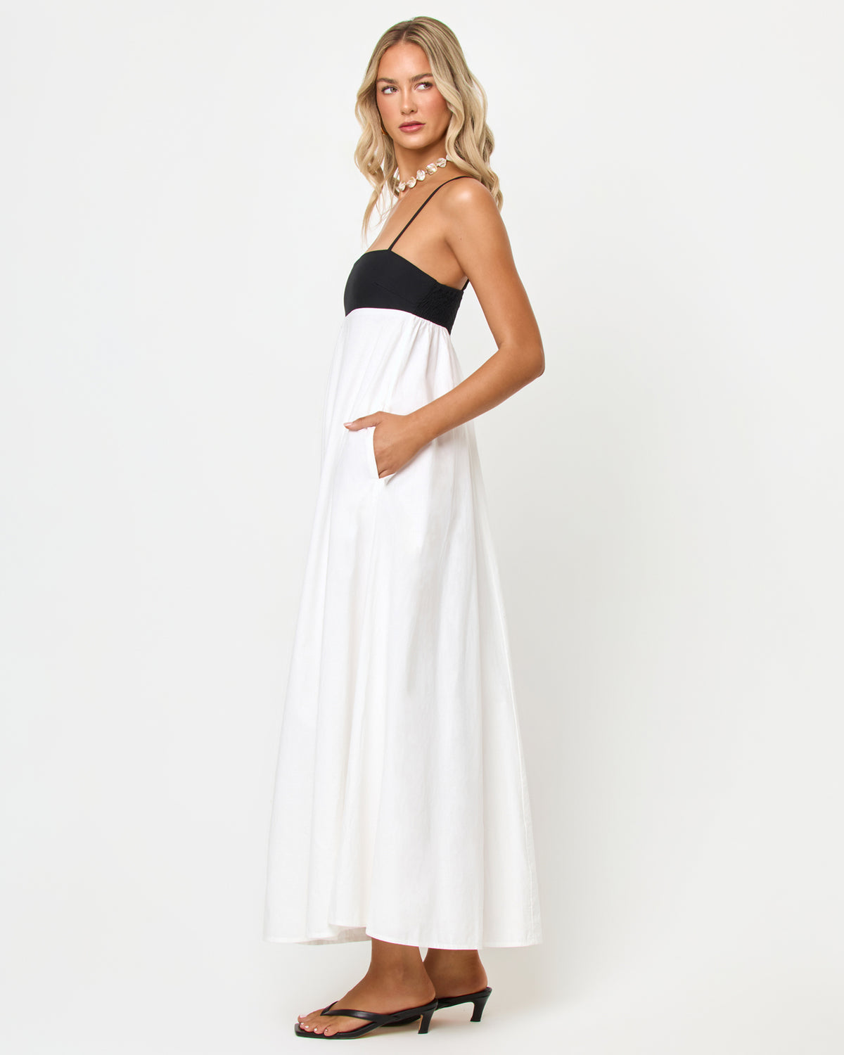 Raveena Dress - Black-Cream Side view of a model wearing the LSPACE Raveena Dress in black-cream, showing the empire-waist silhouette with a black bodice, spaghetti straps, and a flowing cream maxi skirt.