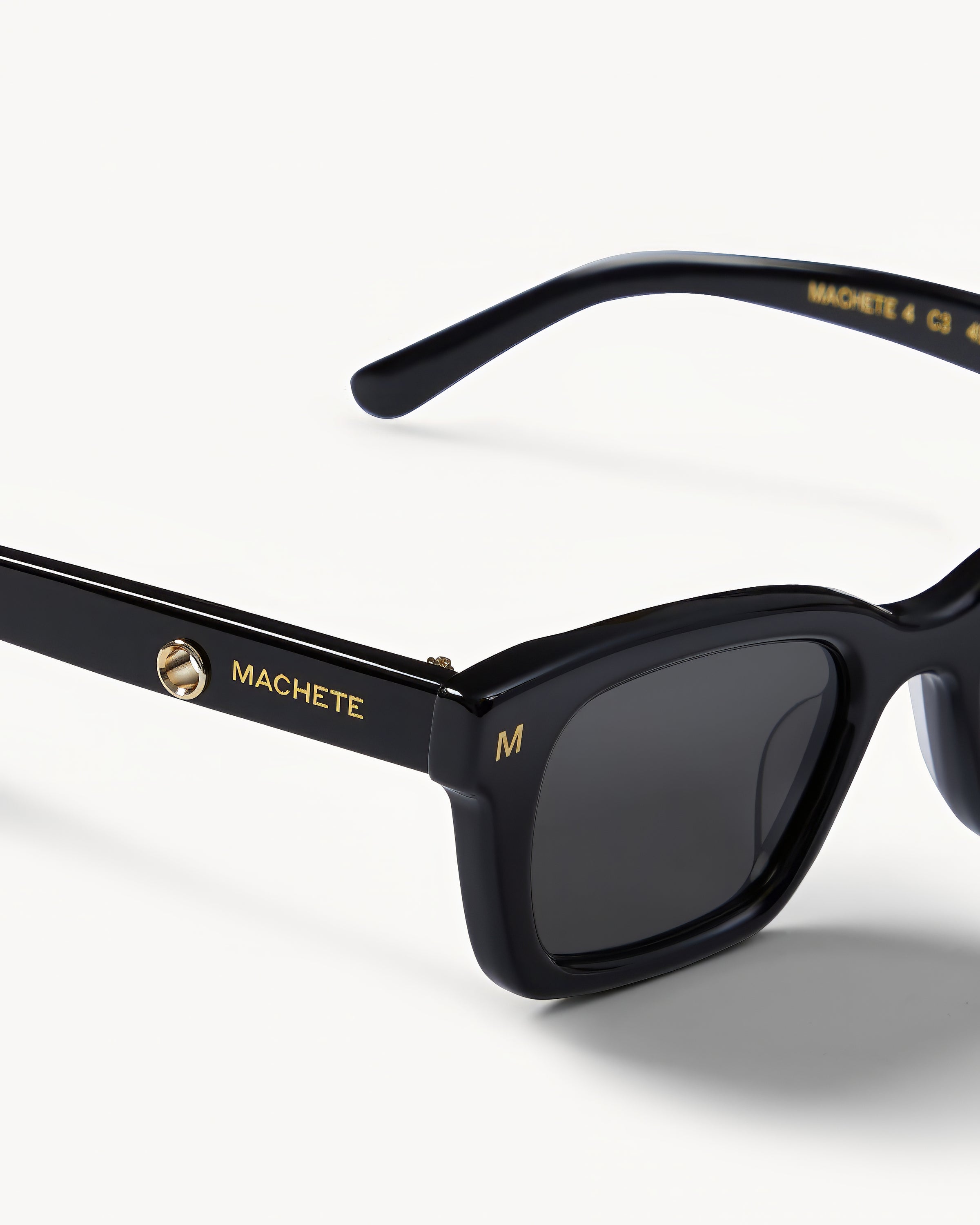 Machete Ruby Sunglasses - Black Close-up detail of the Machete Ruby Sunglasses in black showing the Machete branding on the temple arm and dark grey lenses.