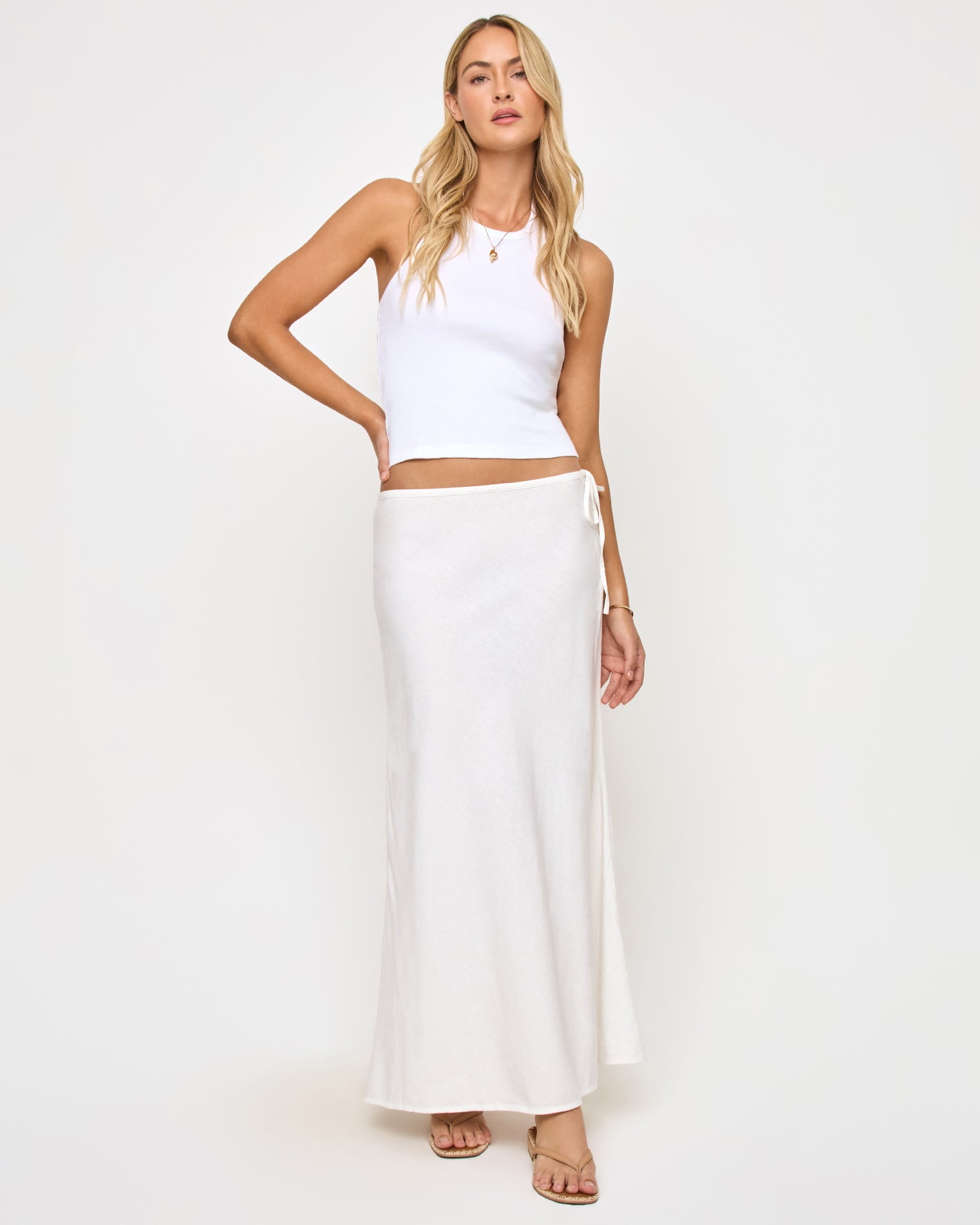 Stop and Stare Skirt - Cream Front view of a model wearing the LSPACE Stop and Stare Skirt in cream, a flowing maxi skirt with a low waist and side tie button closure, styled with a white halter crop top.