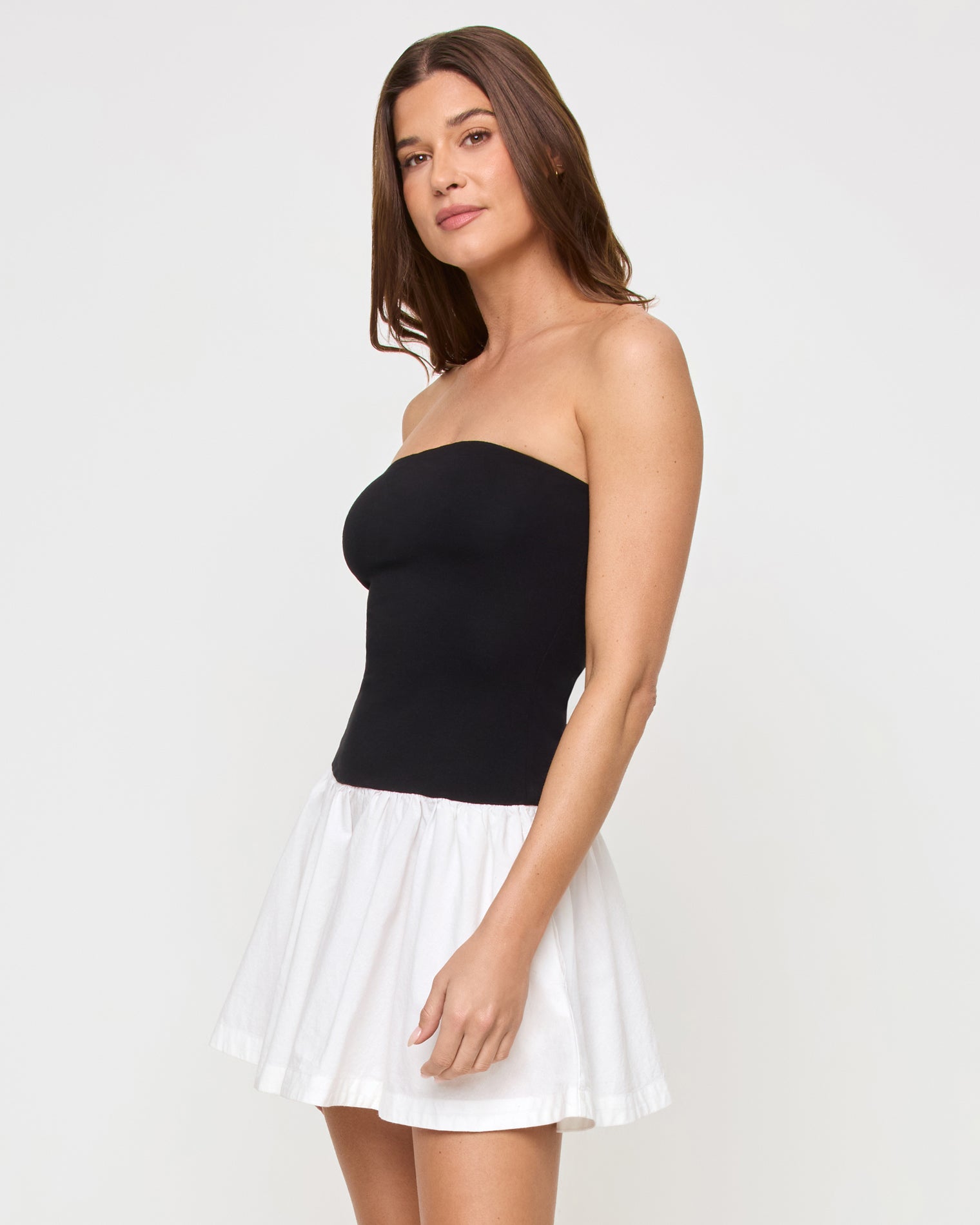 Sienna Mini Dress - Black-Cream Side view of a model wearing the LSPACE Sienna Mini Dress in black-cream, highlighting the contrast between the fitted black strapless bodice and the voluminous cream ruffled skirt.
