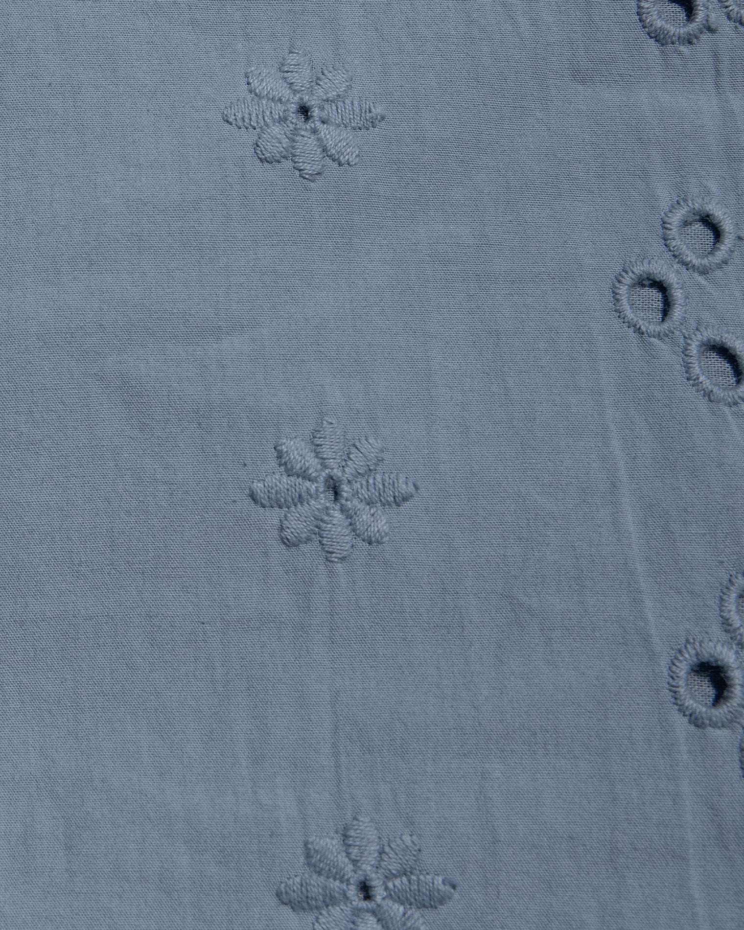 Sunday Mini - Chambray Close-up of a dusty blue fabric with embroidered floral motifs and eyelet embroidery.