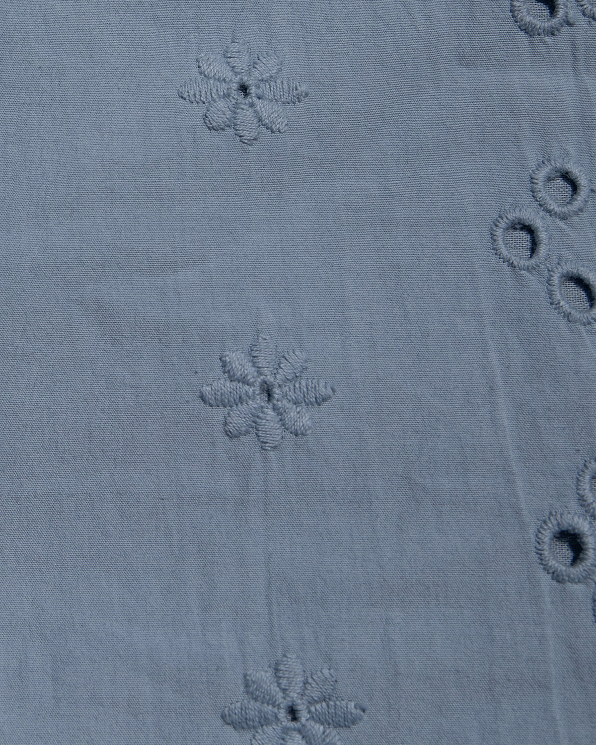 Sunday Mini - Chambray Close-up of a dusty blue fabric with embroidered floral motifs and eyelet embroidery.