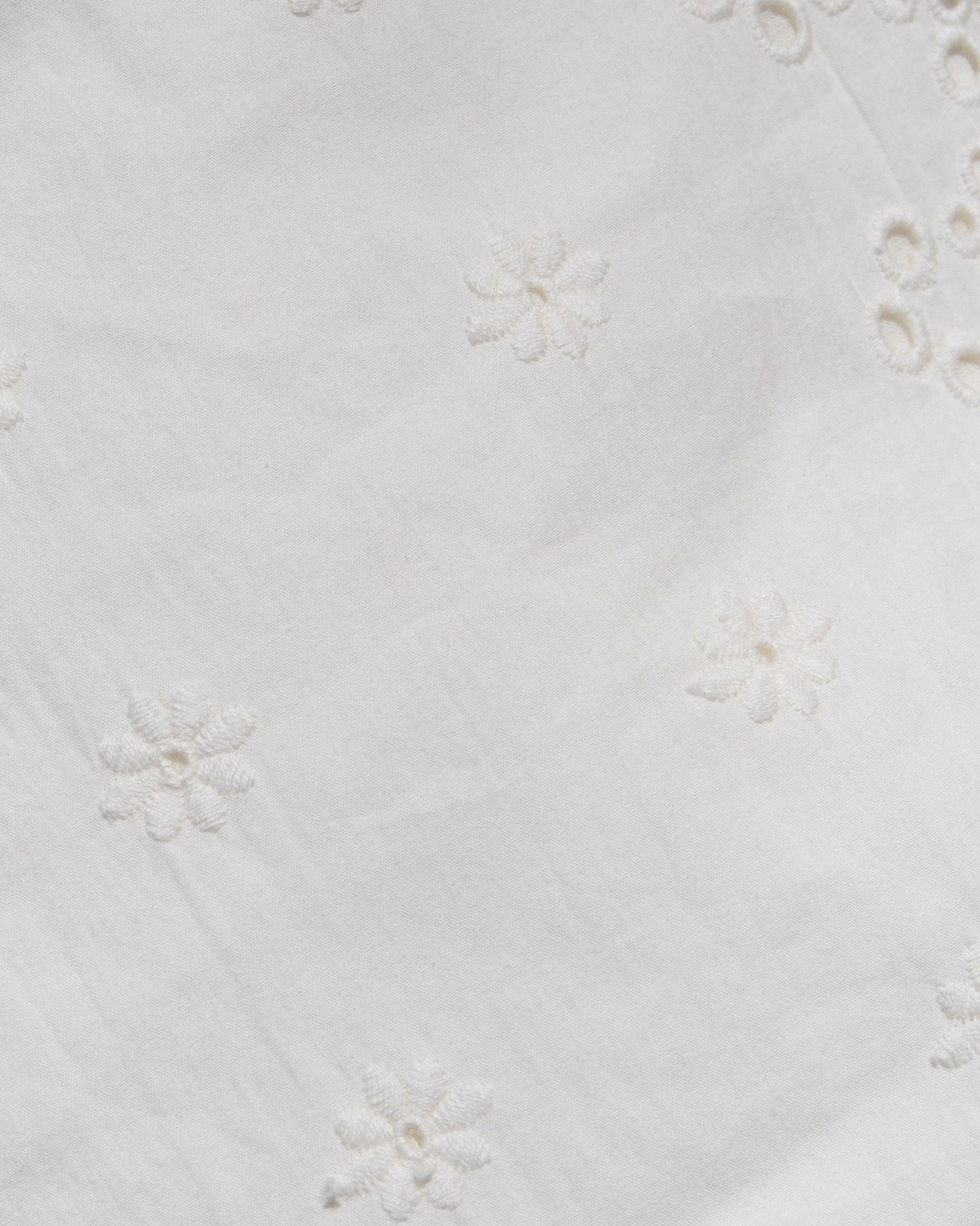 Sunday Mini - Cream Close-up of a white fabric with delicate floral eyelet embroidery and small cutout details.