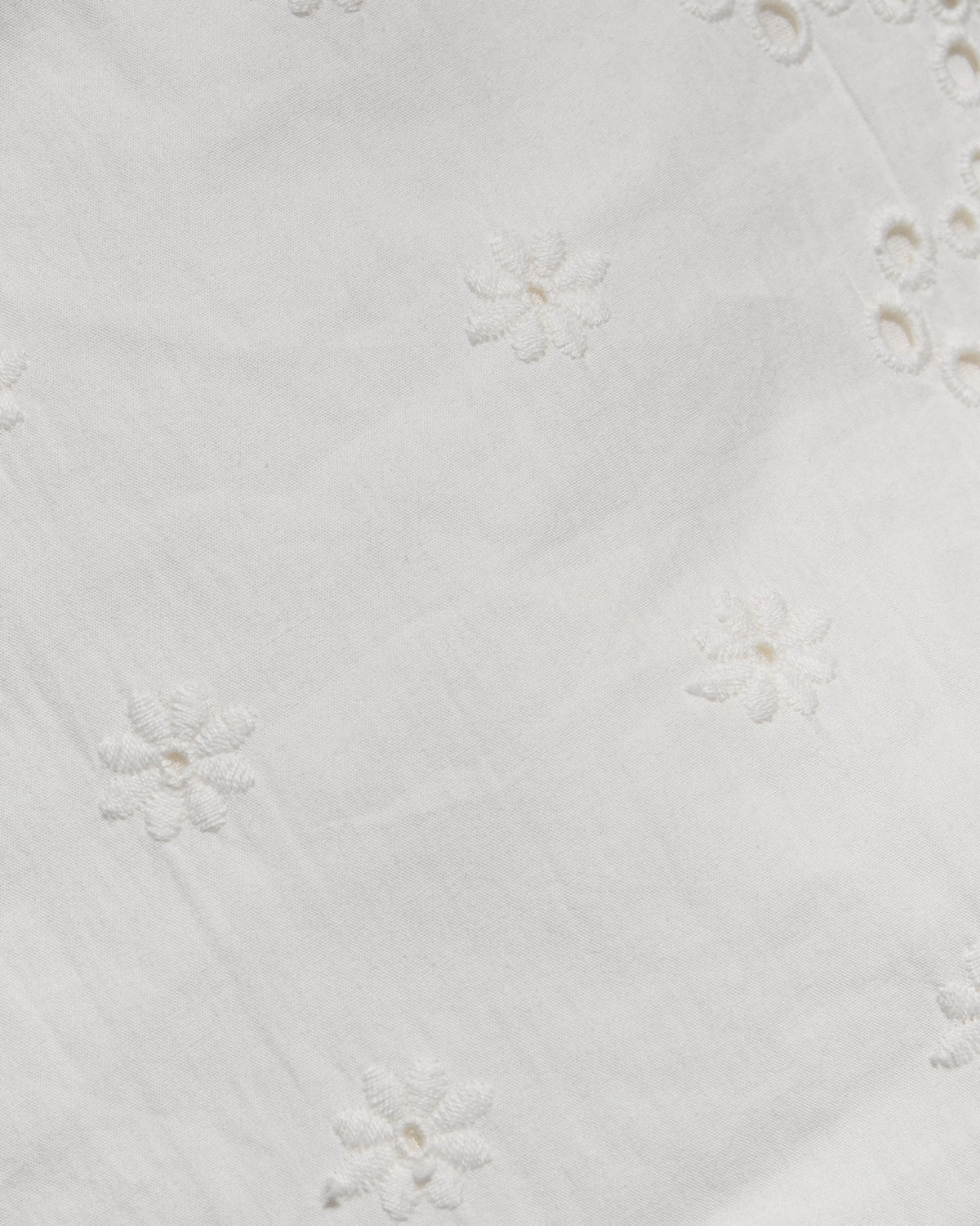 Sunday Mini - Cream Close-up of a white fabric with delicate floral eyelet embroidery and small cutout details.