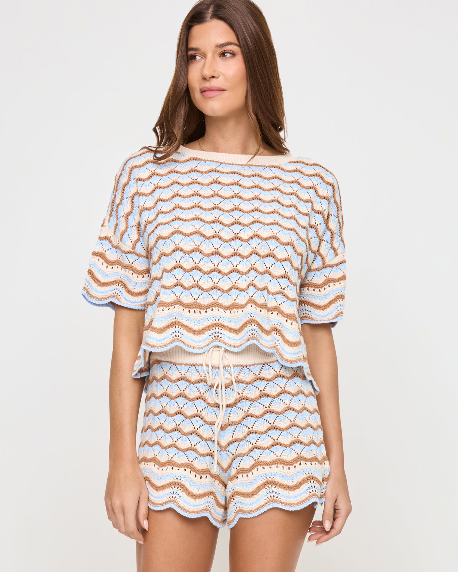 Sunchaser Top - North Shores Angled front view of a model wearing the LSPACE Sunchaser Top in north shores, a boxy crochet knit top with a wave scallop pattern in light blue and tan, paired with the coordinating shorts.