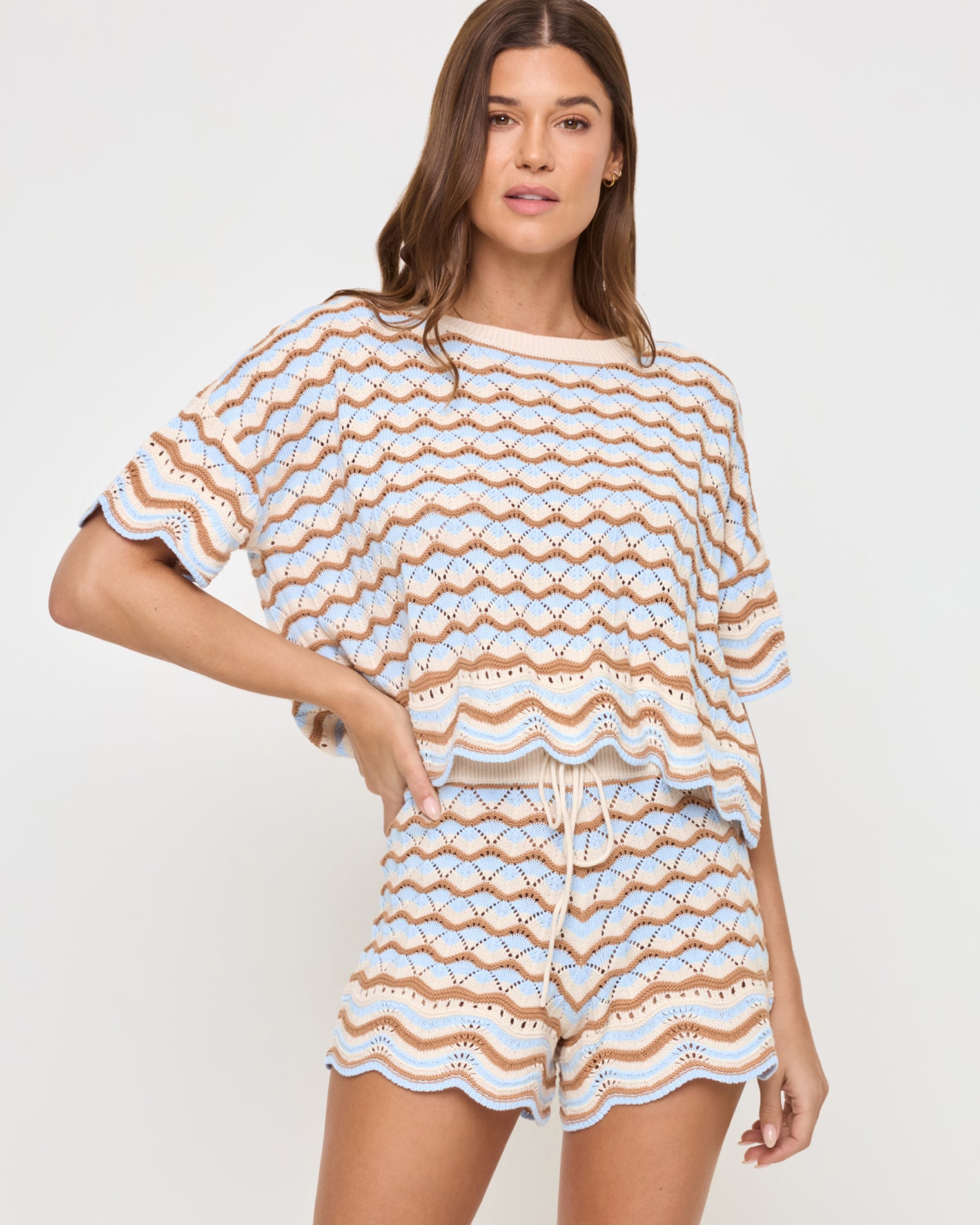 Sunchaser Top - North Shores Front view of a model wearing the LSPACE Sunchaser Top in north shores, featuring a relaxed boxy fit, short sleeves, and a wave scallop crochet pattern in light blue and tan, styled with the matching shorts.