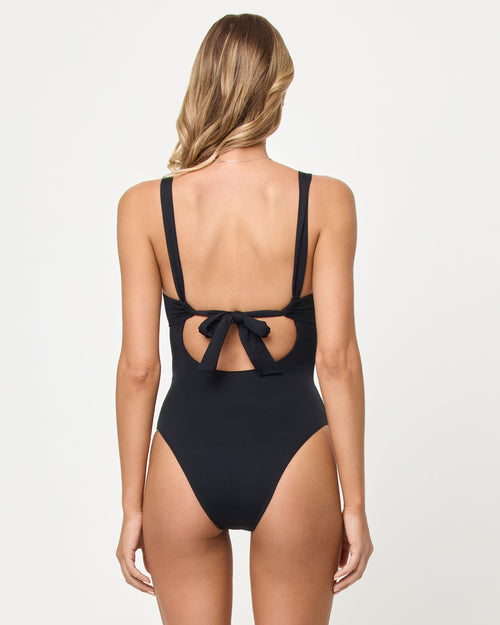Back view of a model wearing the LSPACE black Delano One Piece with an open back and tie detail.