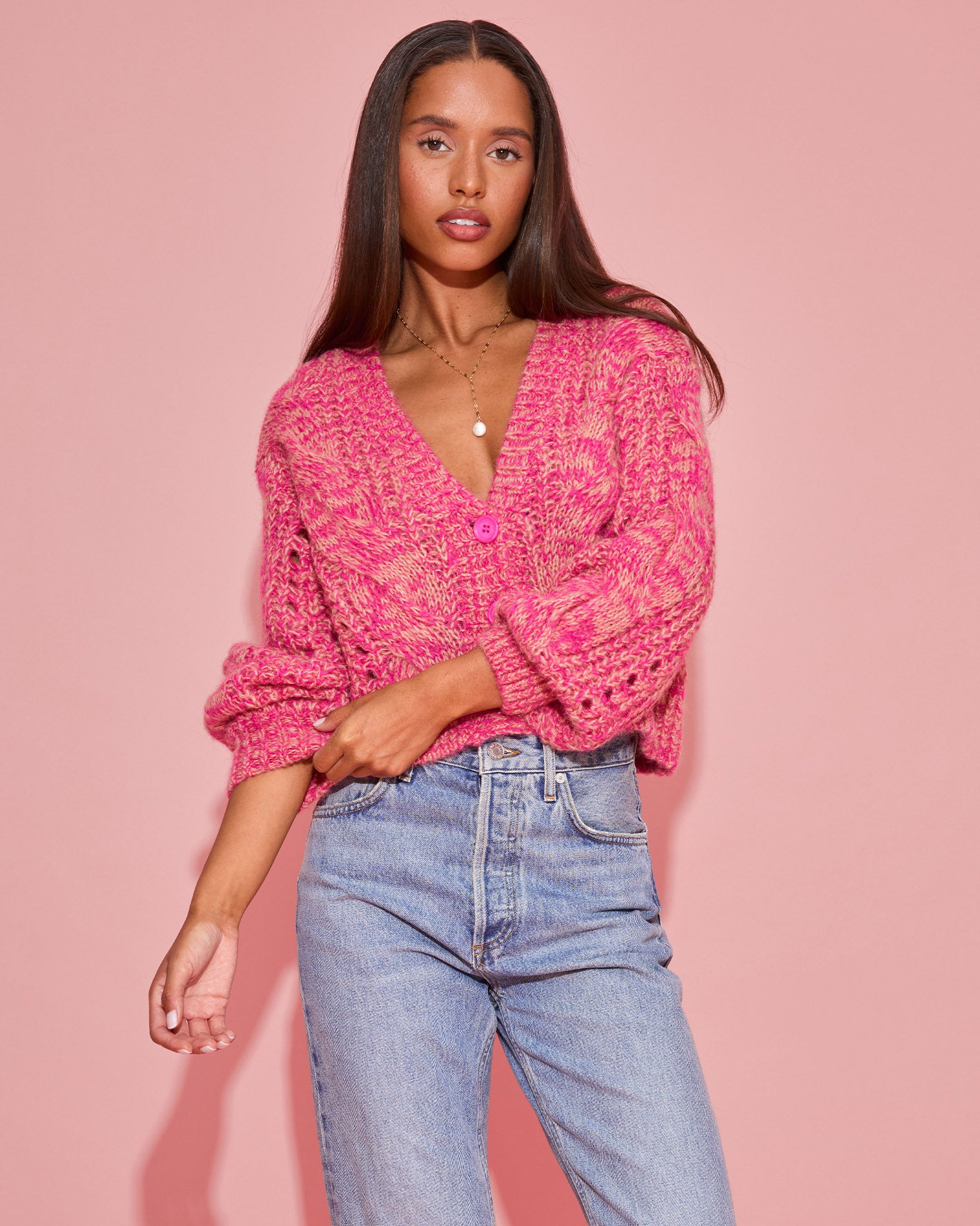 Strawberry Fields Cardigan - Strawberry Marl Close-up front view of a model wearing the LSPACE Strawberry Fields Cardigan in strawberry marl, showing the pink marl cable-knit texture and V-neckline against a pink background.