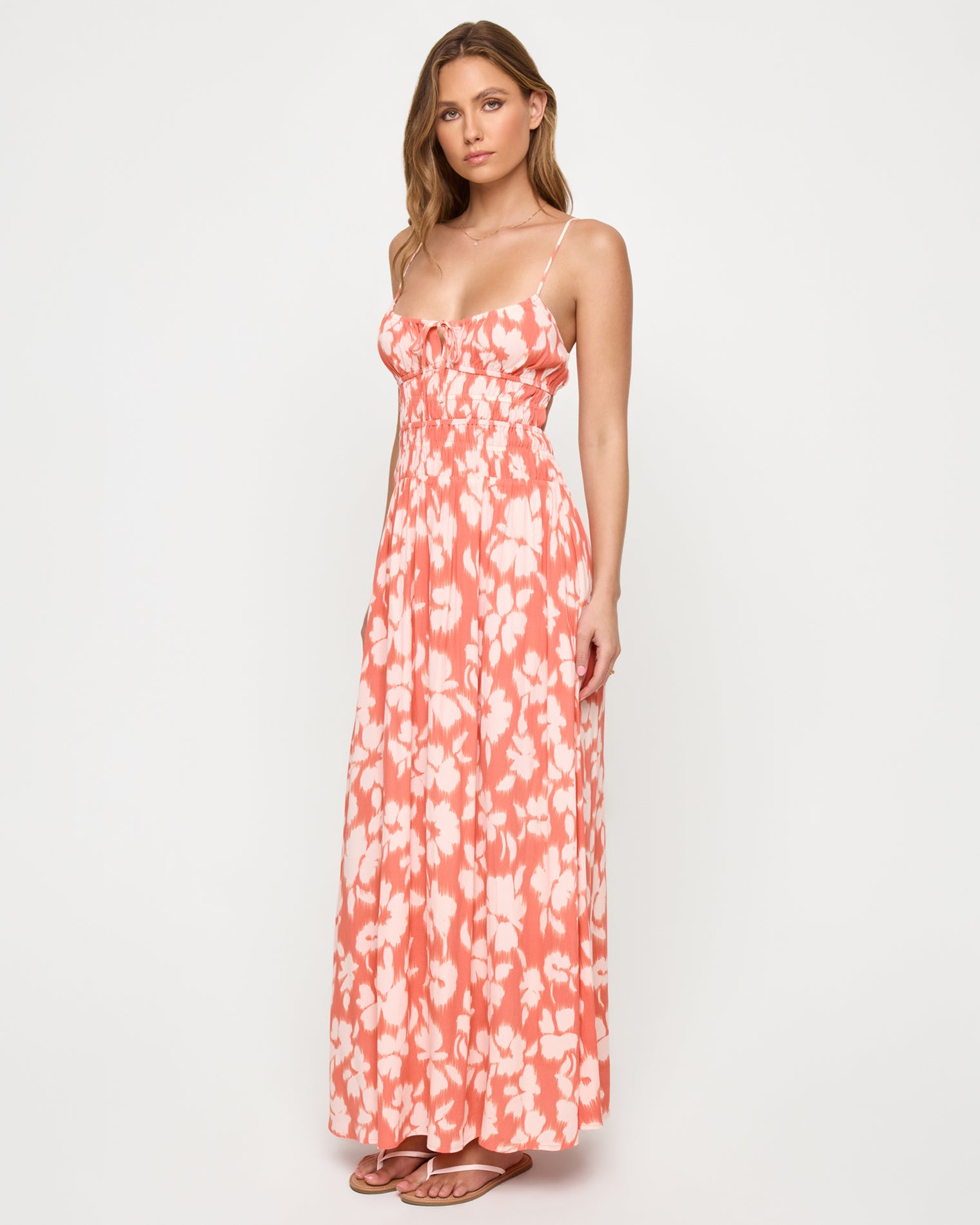 Tala Dress - Vine Vignette Three-quarter front view of a model wearing the LSPACE Tala Dress in vine vignette, showing the spaghetti straps, front tie bodice detail, and flowing maxi skirt in a coral and white floral print.