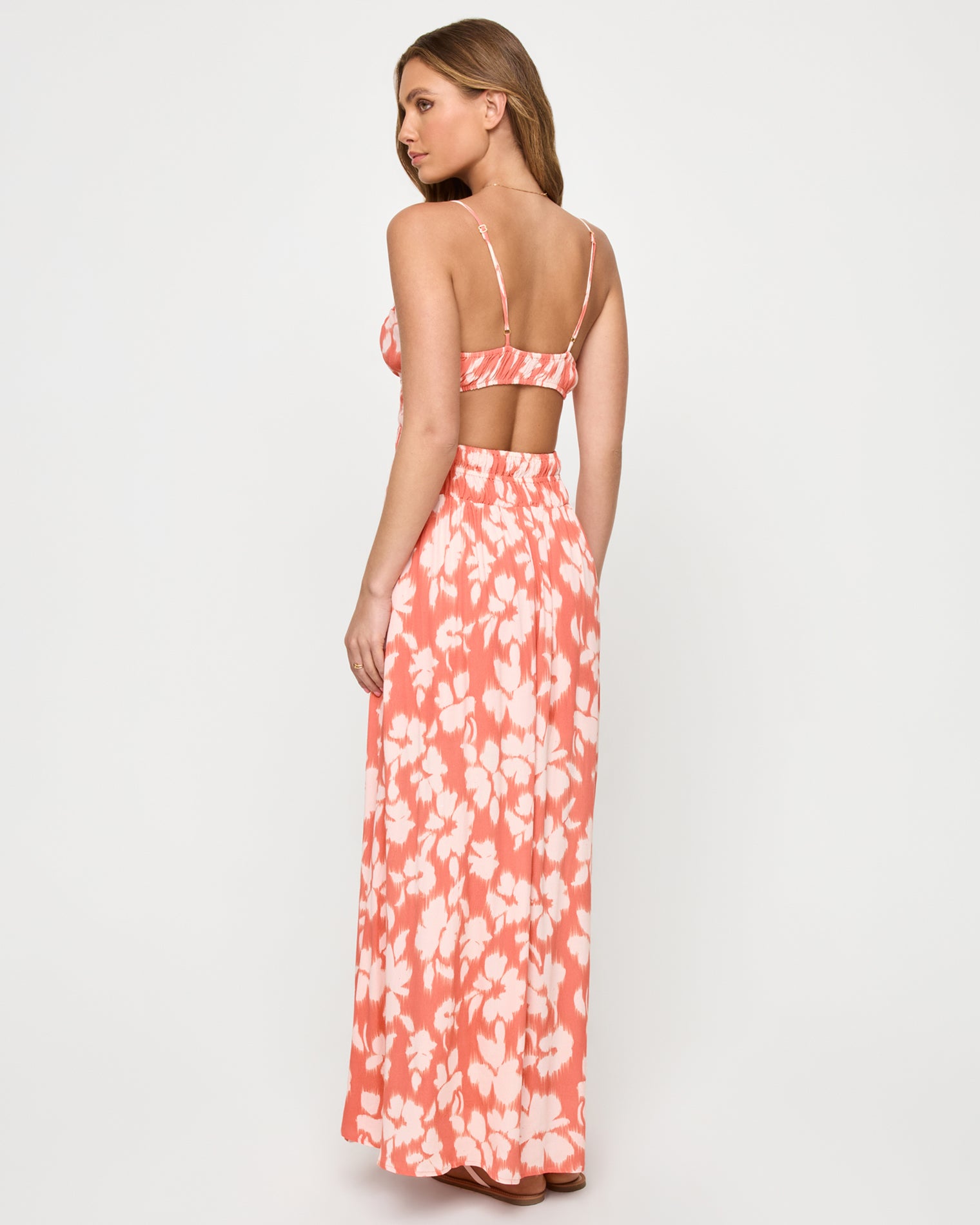 Tala Dress - Vine Vignette Back view of a model wearing the LSPACE Tala Dress in vine vignette, showing the open back with spaghetti straps and an open back cutout above the smocked waist in a coral and white floral print.