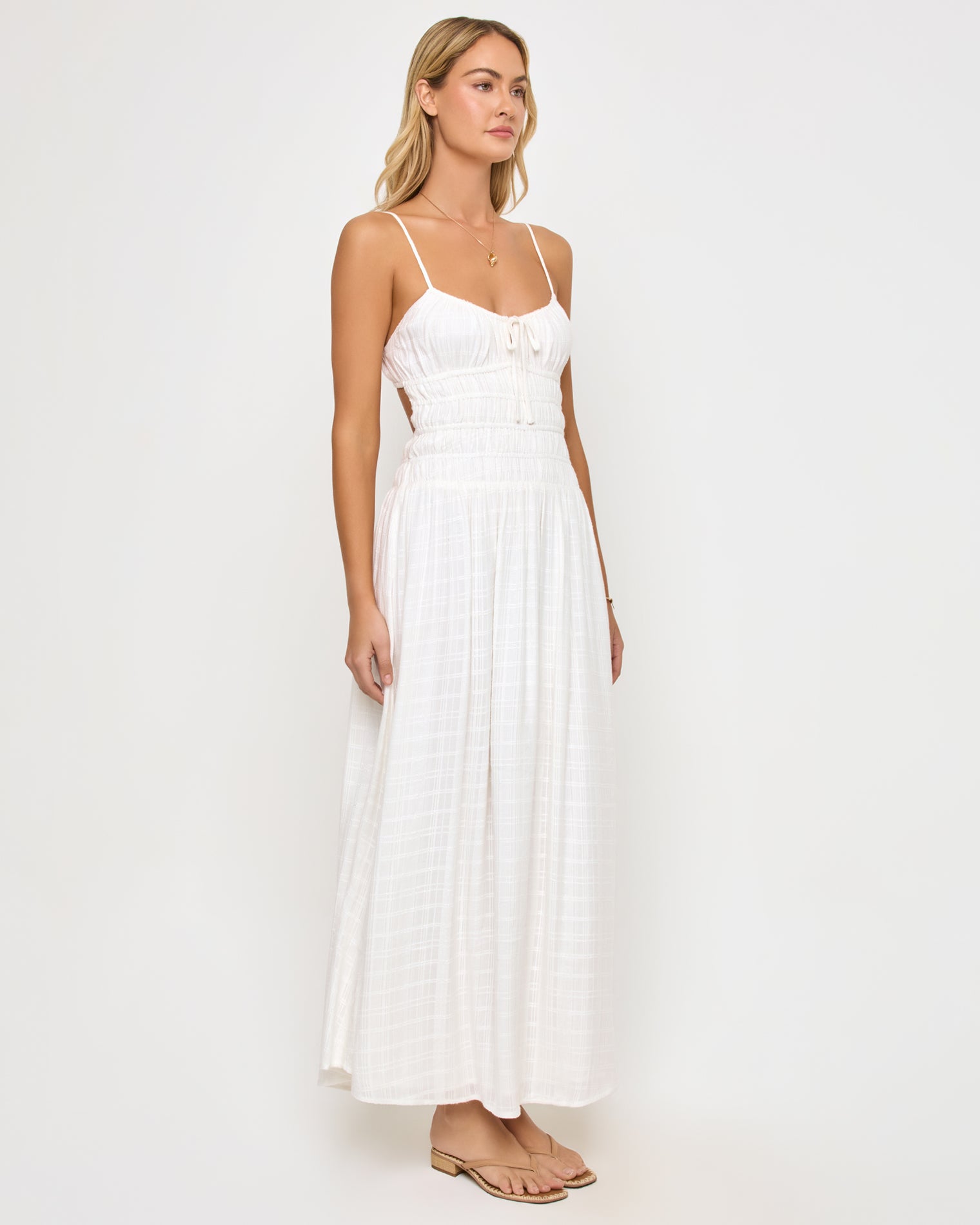 Tala Dress - Cream Angled view of a model wearing the LSPACE Tala Dress in cream, showing the open-back cutout design and the flowing off-white textured maxi skirt from the side.