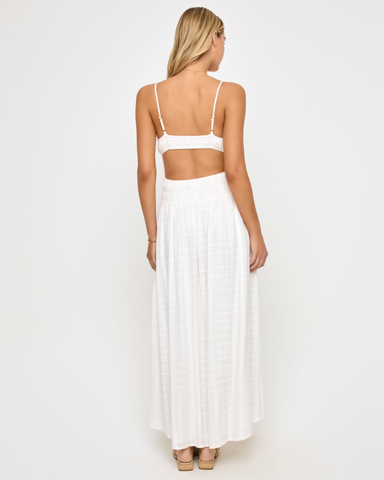 Tala Dress - Cream Back view of a model wearing the LSPACE Tala Dress in cream, showing the wide open-back cutout between the crop-style bodice and smocked waistband of the off-white maxi dress.