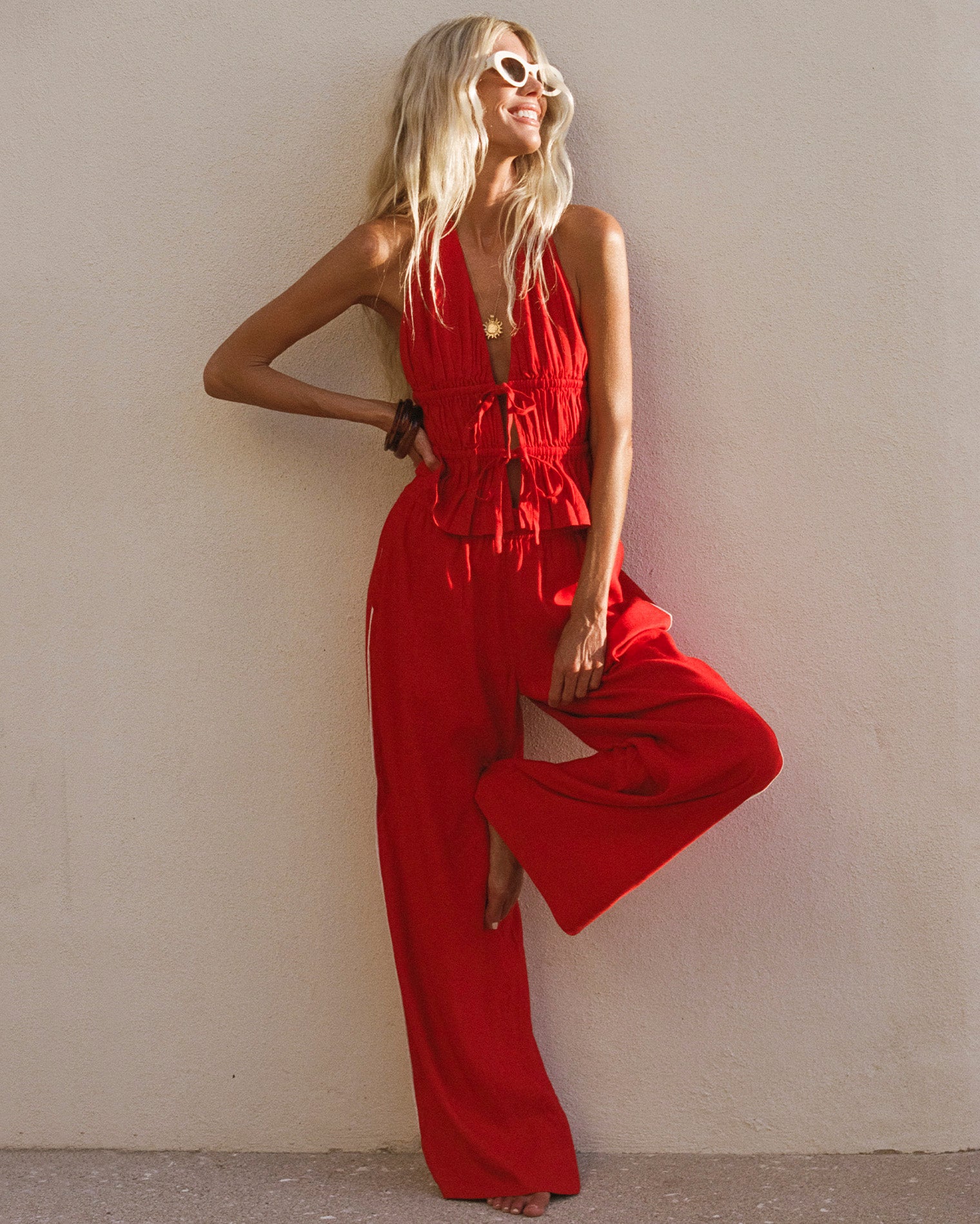 x The Salty Blonde Sur Pant - Flame-Cream Front view of a model wearing the LSPACE x The Salty Blonde Sur Pant in flame-cream, wide-leg flowy pants in flame red with a cream side-seam stripe, styled with a matching red halter top in an outdoor setting.