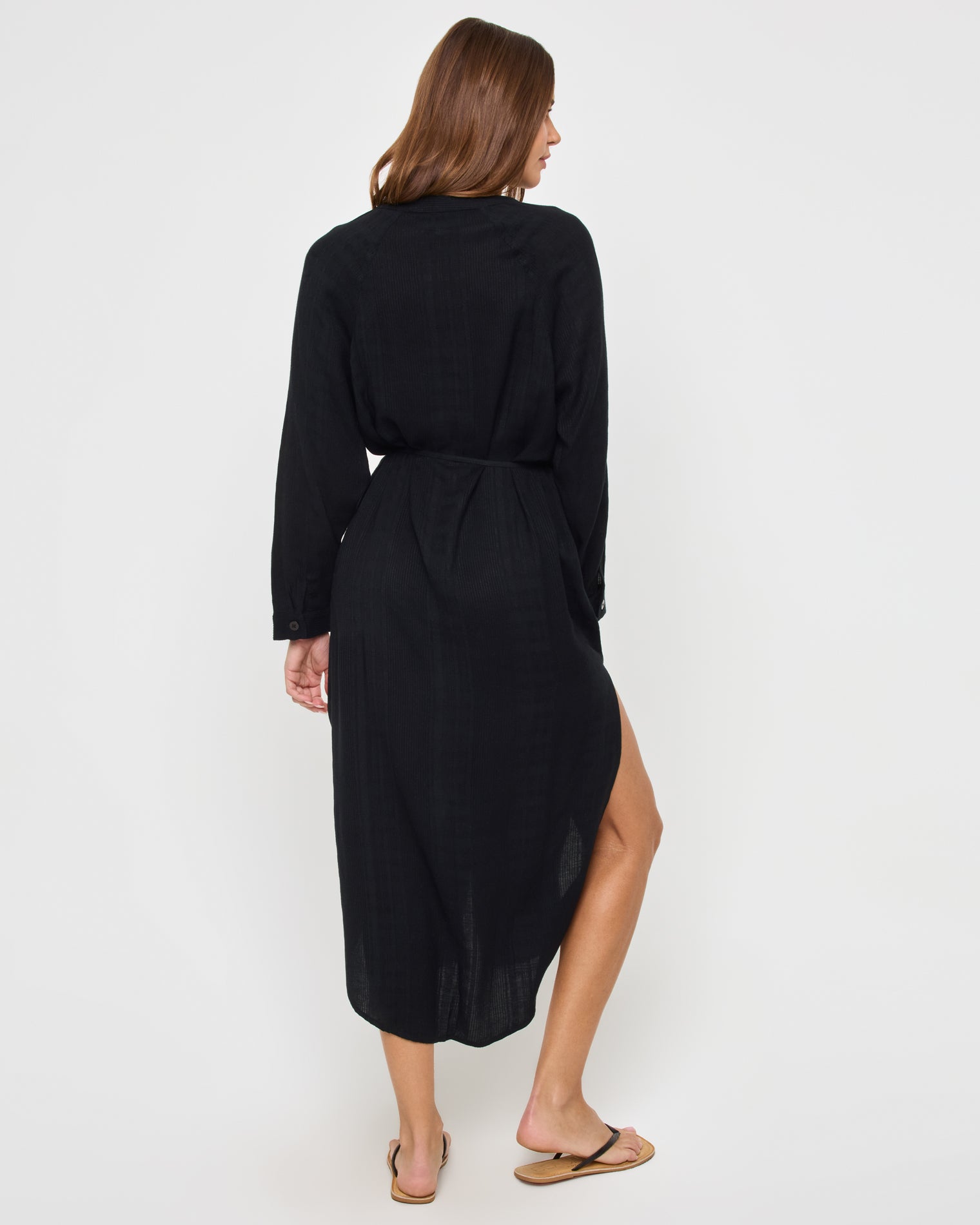 Yoli Shirtdress - Black Back view of a model wearing the LSPACE Yoli Shirtdress in black, showing the full-length back of the midi shirtdress with the drawstring waist and the high-low hemline.
