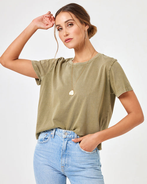 Front view of a model wearing the LSPACE All Day Top in olive branch with one arm raised, styled with light wash jeans.