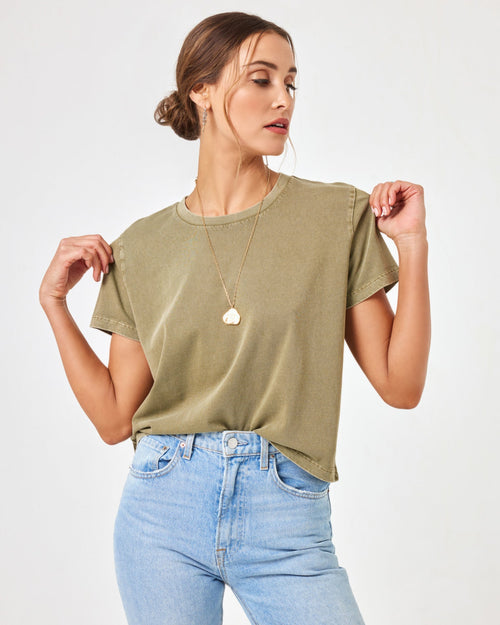 Front view of a model holding the LSPACE All Day Top in olive branch at the shoulders, styled with light wash jeans.