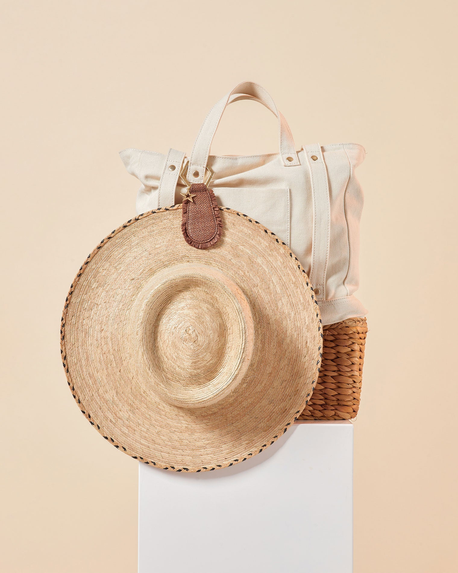 LSPACE x Lindsay Albanese TOPTOTE - Tobacco Off-model image of the LSPACE x Lindsay Albanese TOPTOTE clipped to a canvas tote bag alongside a straw hat on a white pedestal.