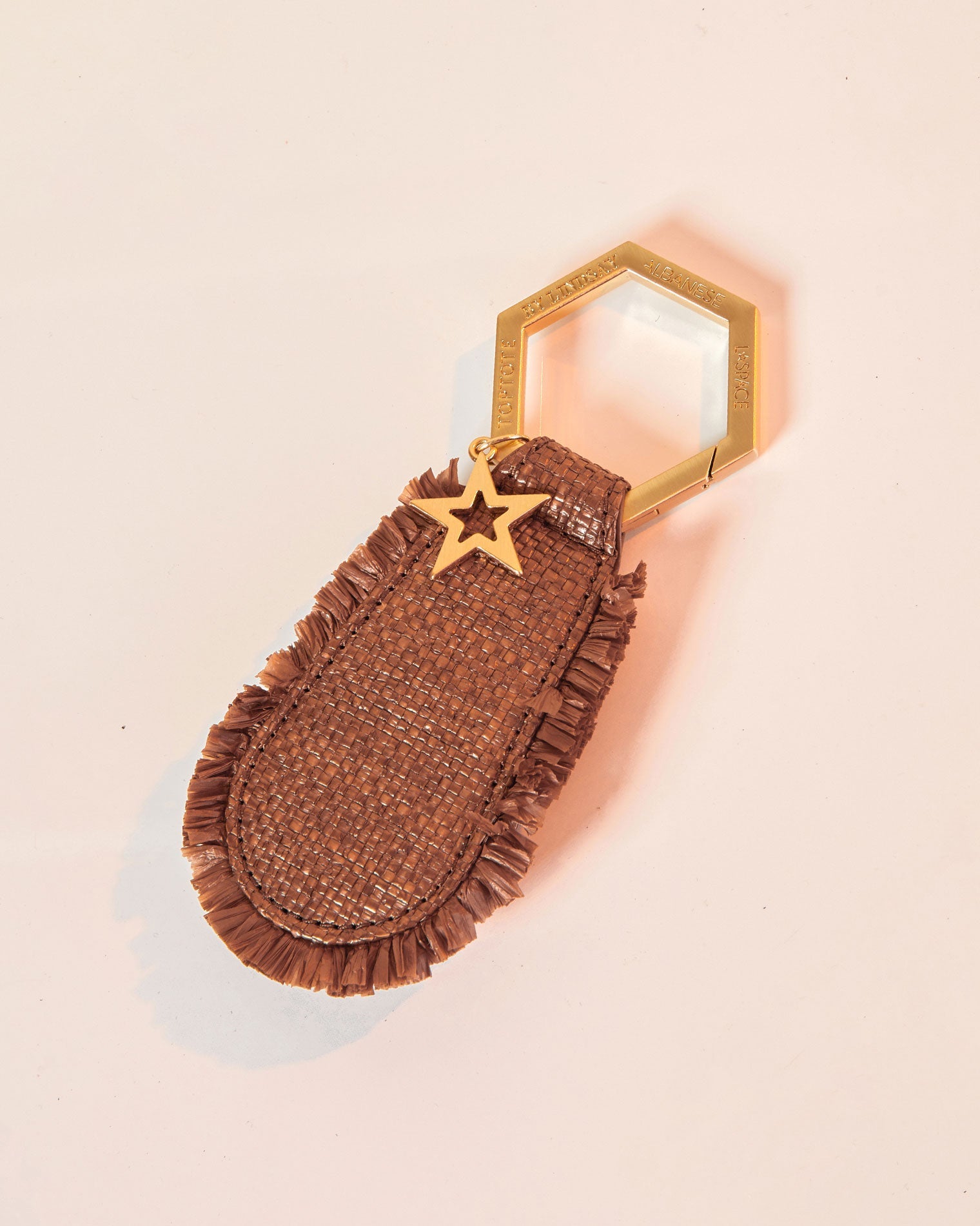 LSPACE x Lindsay Albanese TOPTOTE - Tobacco Off-model image of the LSPACE x Lindsay Albanese TOPTOTE in tobacco showing the woven raffia body with fringe trim, gold hexagonal carabiner ring, and star charm.